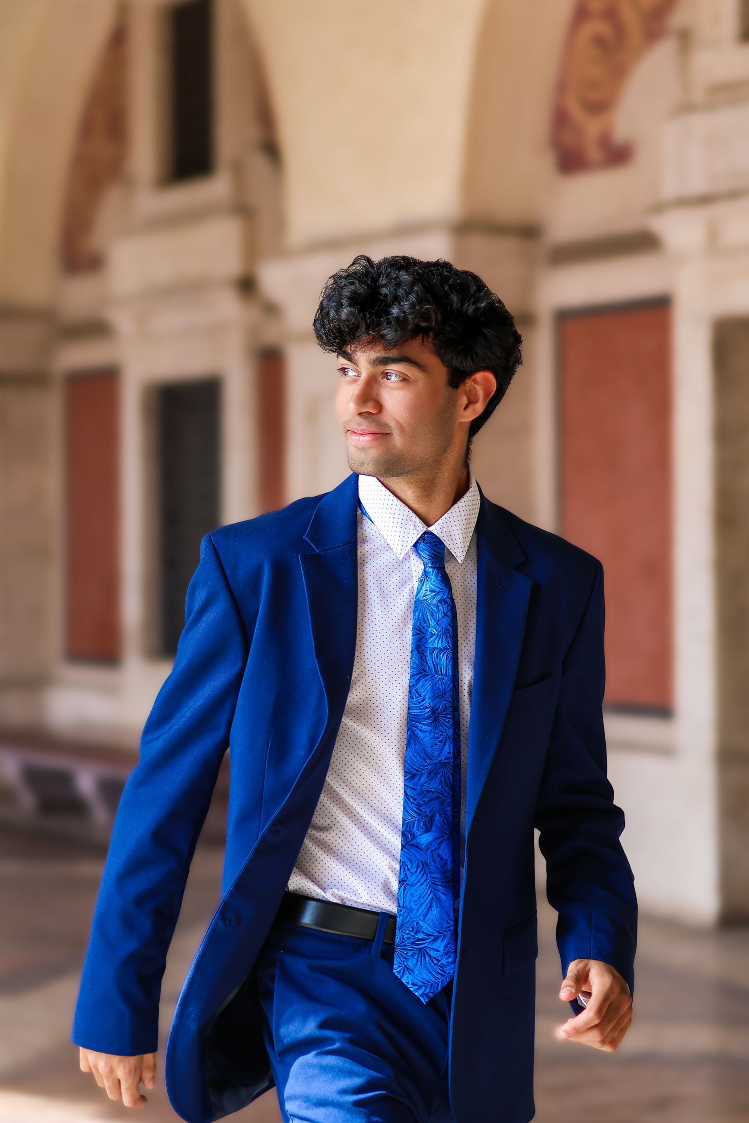 A professional wearing a stylish royal blue suit and matching tie stands in an elegant architectural setting.