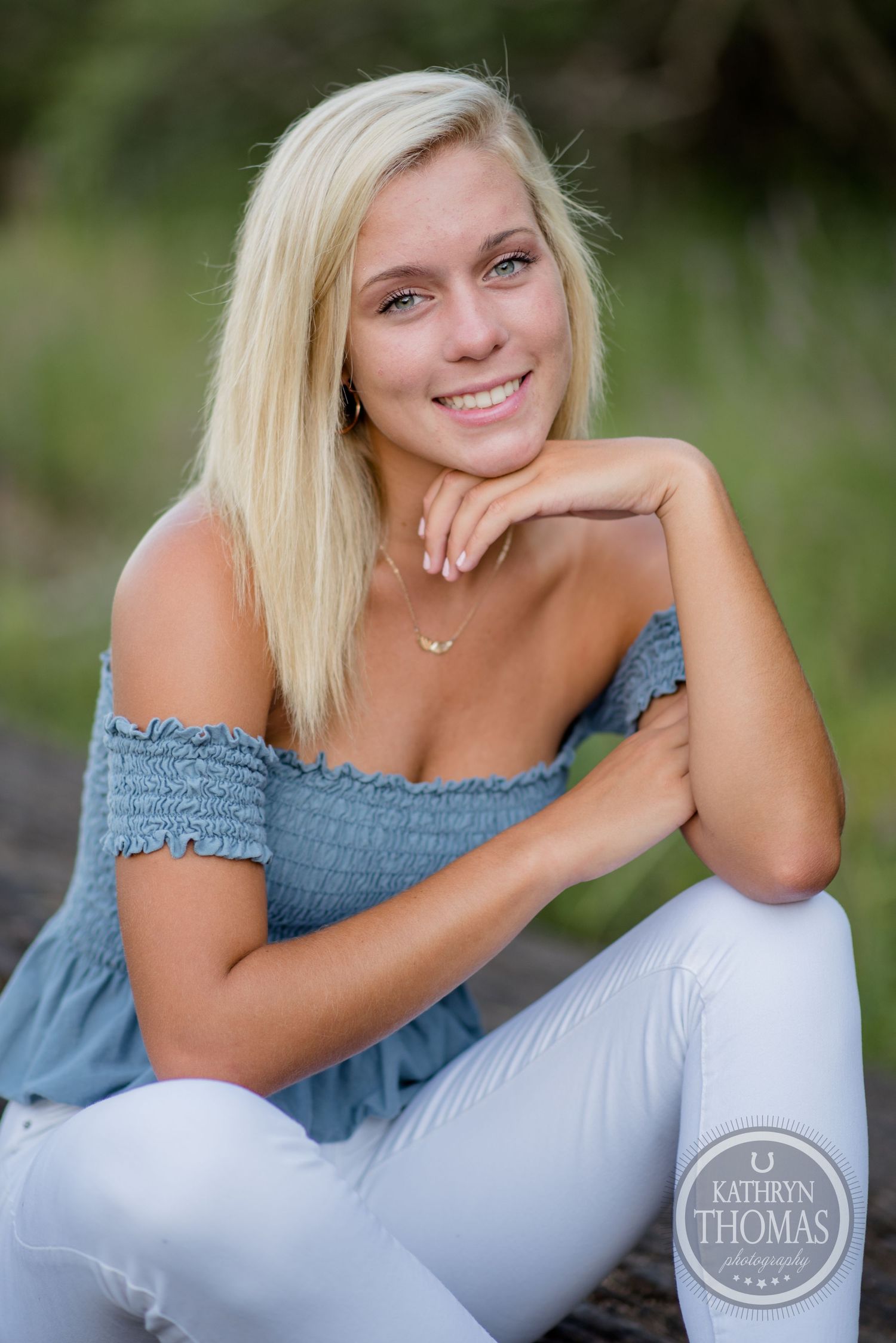 Summer portrait featuring someone in blue off-shoulder top and white pants against natural backdrop.
