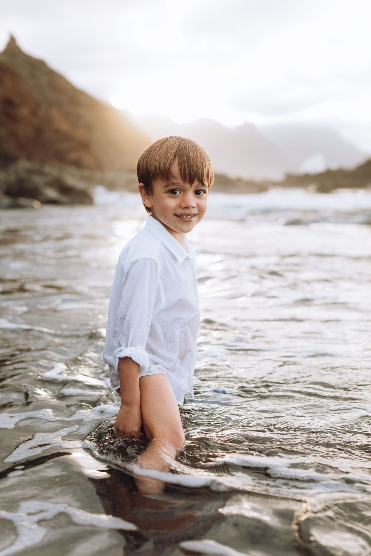 Little boy enjoying the ocean water on his feet while looking at the camera.