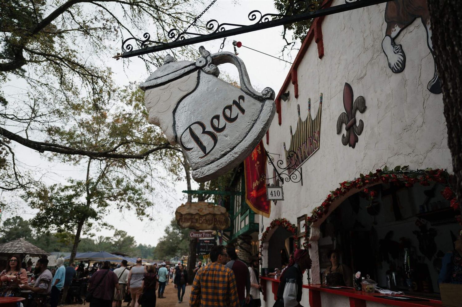 Rustic beer sign hanging outside a medieval-themed tavern or shop at a renaissance festival.
