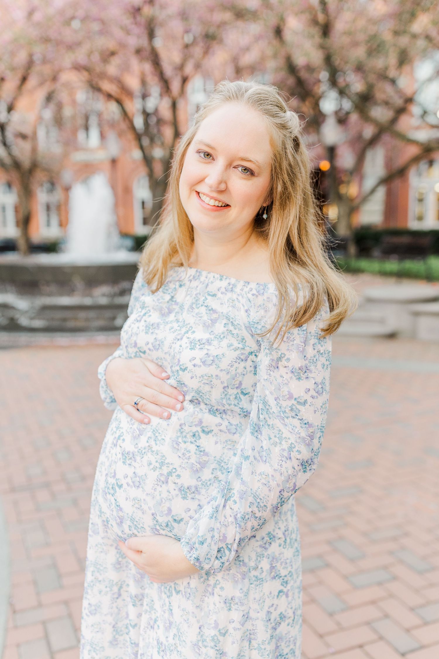 A floral dress being worn in front of blooming cherry trees on a brick courtyard.