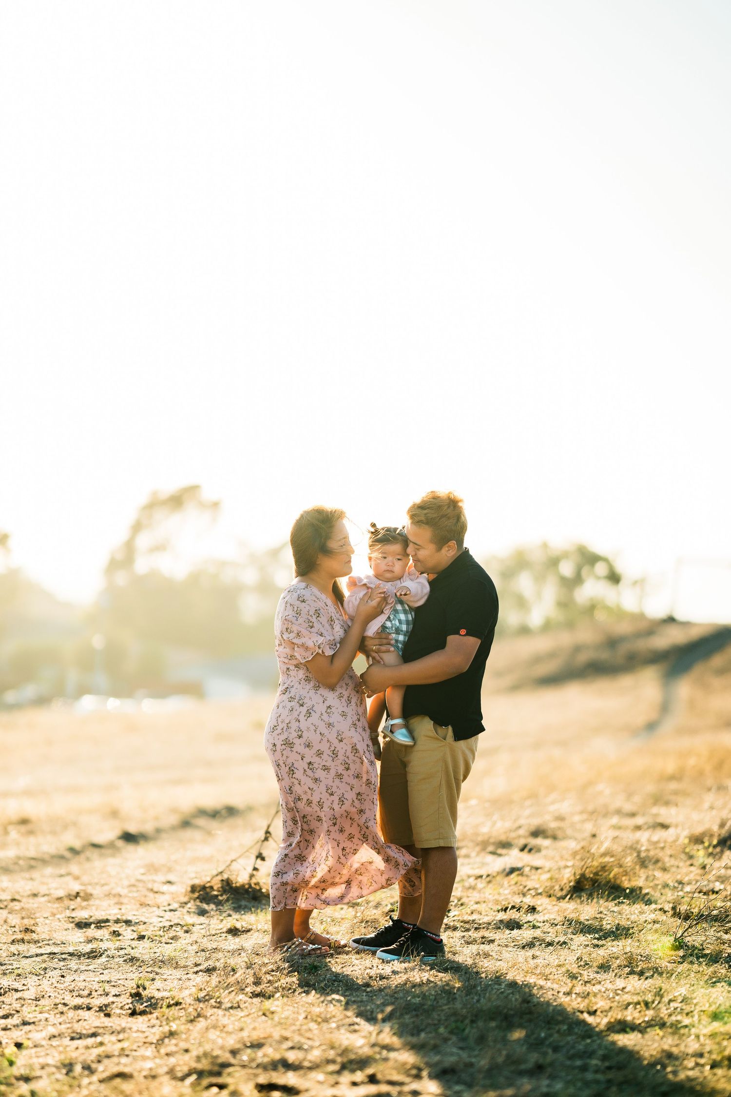 Family enjoying tender moment together during golden sunset on grassy hillside.
