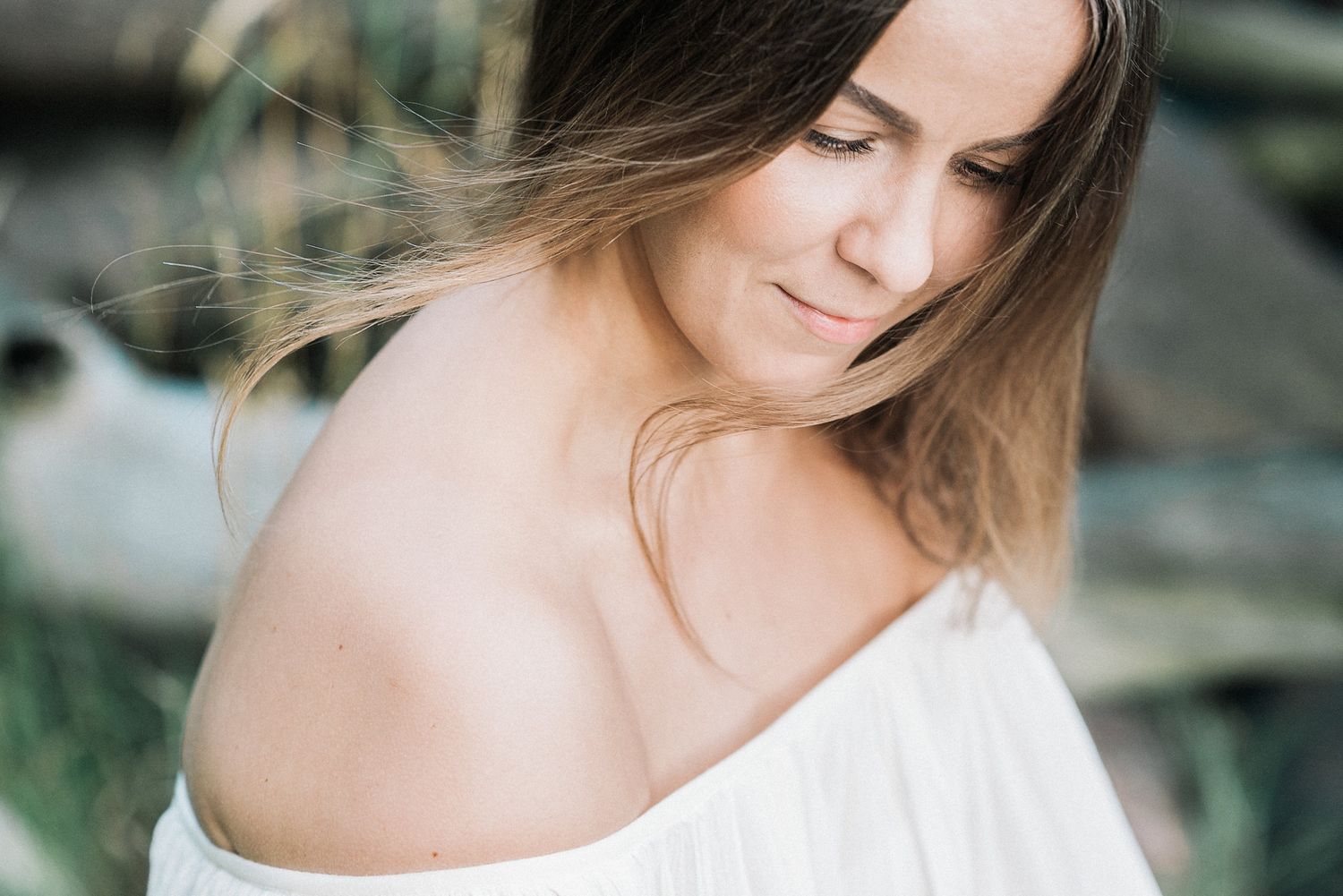 Side profile of a woman in white off-shoulder dress looking down pensively.