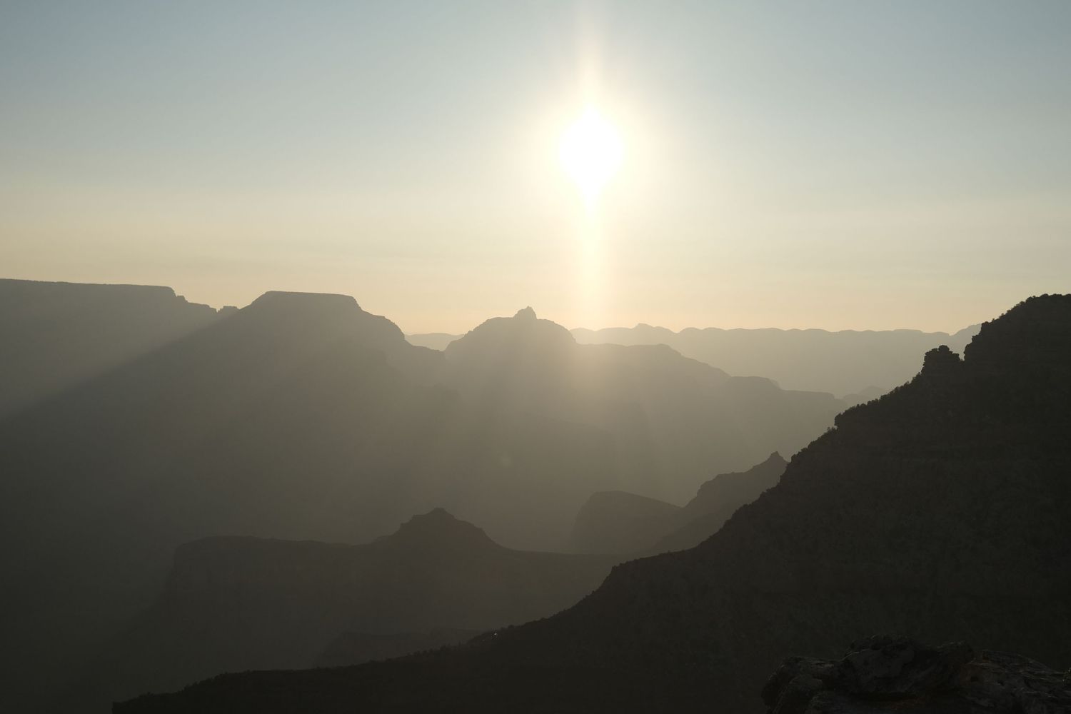Silhouette of mountain ranges at sunset with sun creating dramatic backlighting.