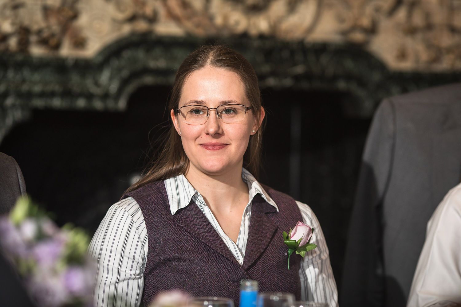 Wedding guest in professional attire smiles warmly at reception.