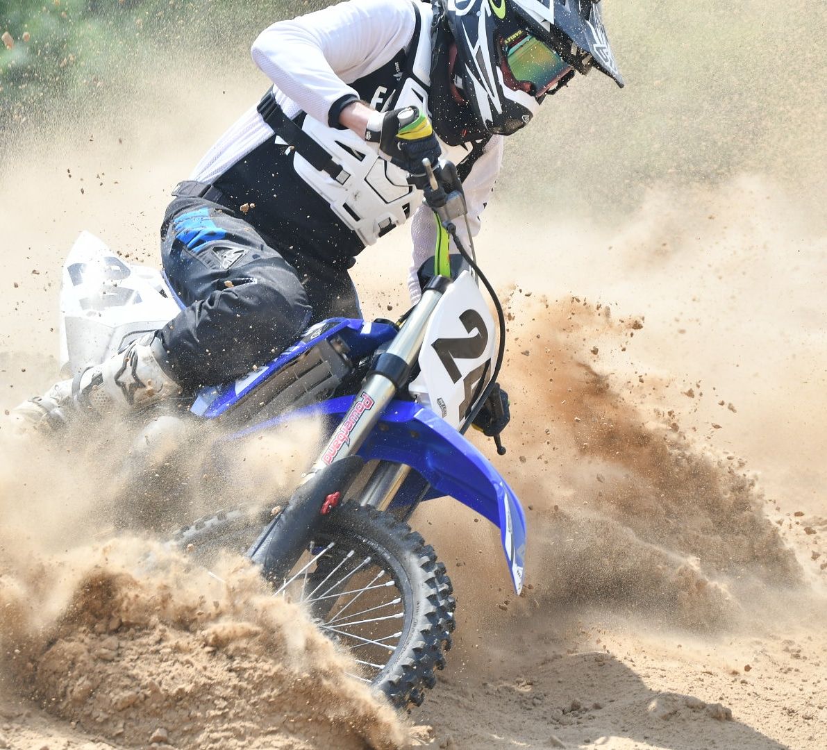 Motocross rider on blue dirt bike kicking up dust during intense race action.