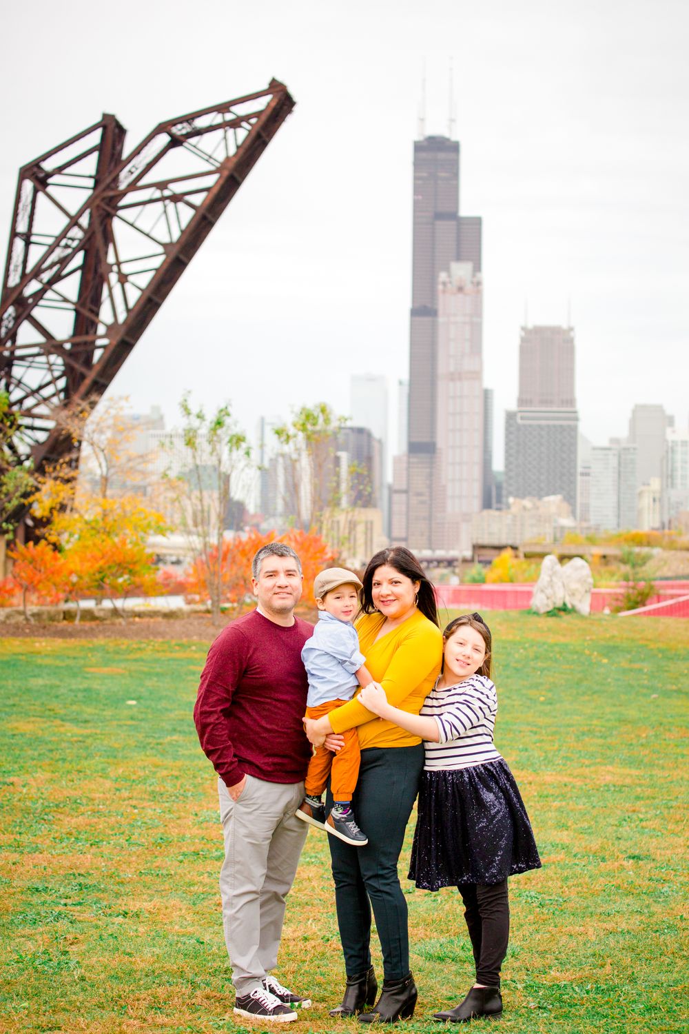 A family of four poses together on autumn grass with the Chicago skyline visible in the background.