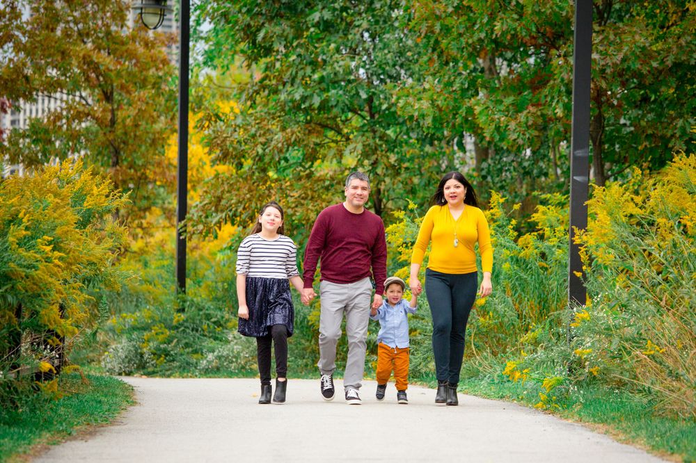 A family walks together on a path surrounded by vibrant yellow fall flowers and greenery.