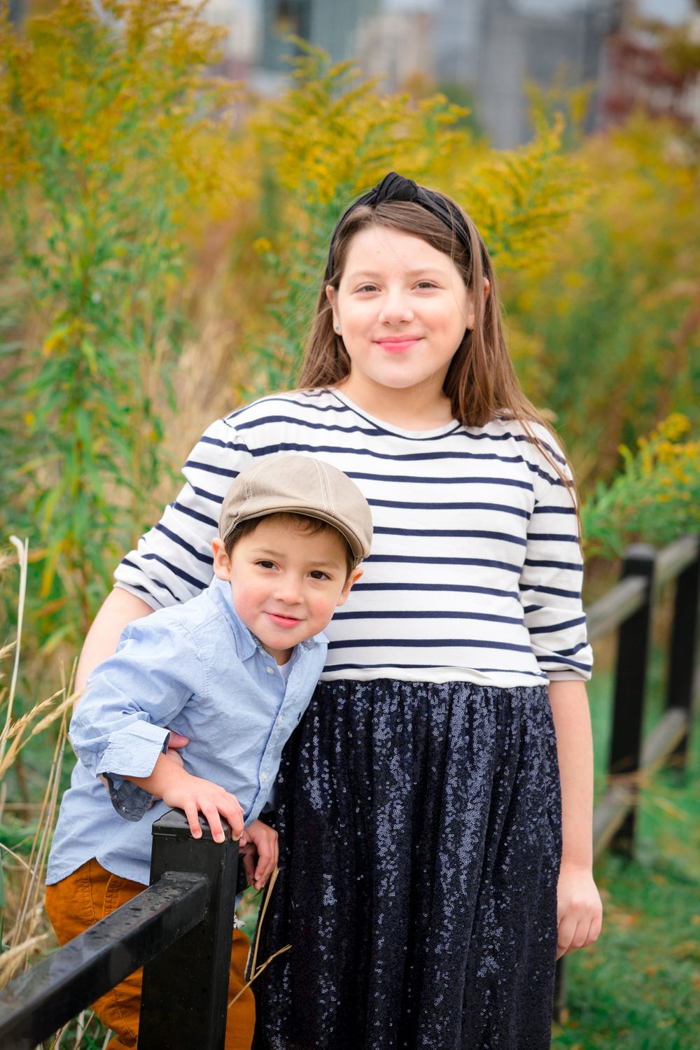 Two people pose together by a railing with golden autumn foliage in the background.