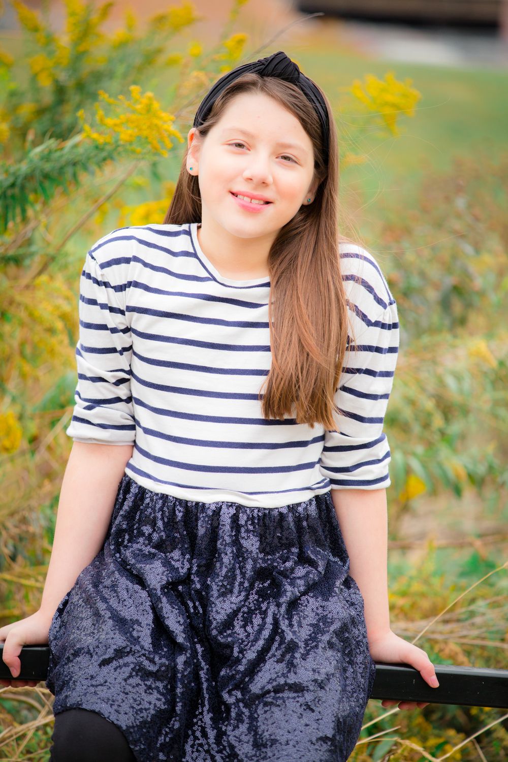 A person in a striped top and navy sequin skirt poses outdoors against autumn foliage.