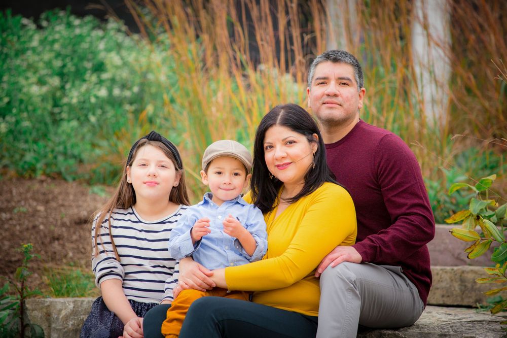 A family of four sits together on stone steps with autumn foliage in the background.