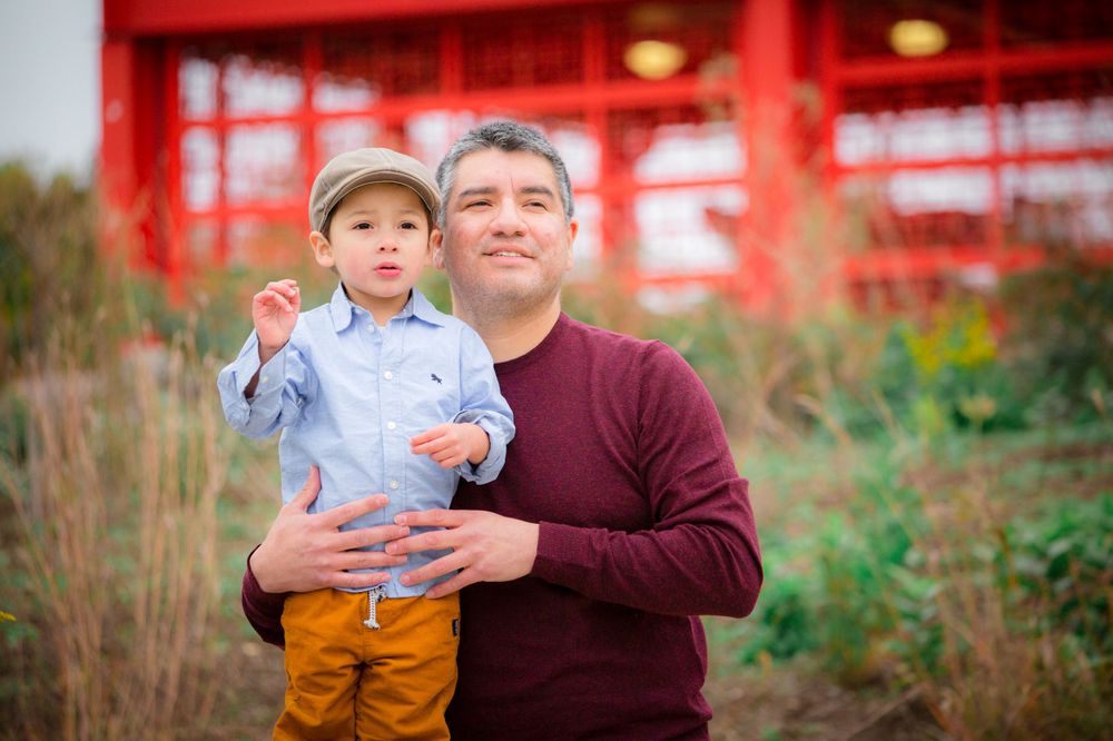 Parent and child pose together in front of red architectural structure in outdoor portrait session.
