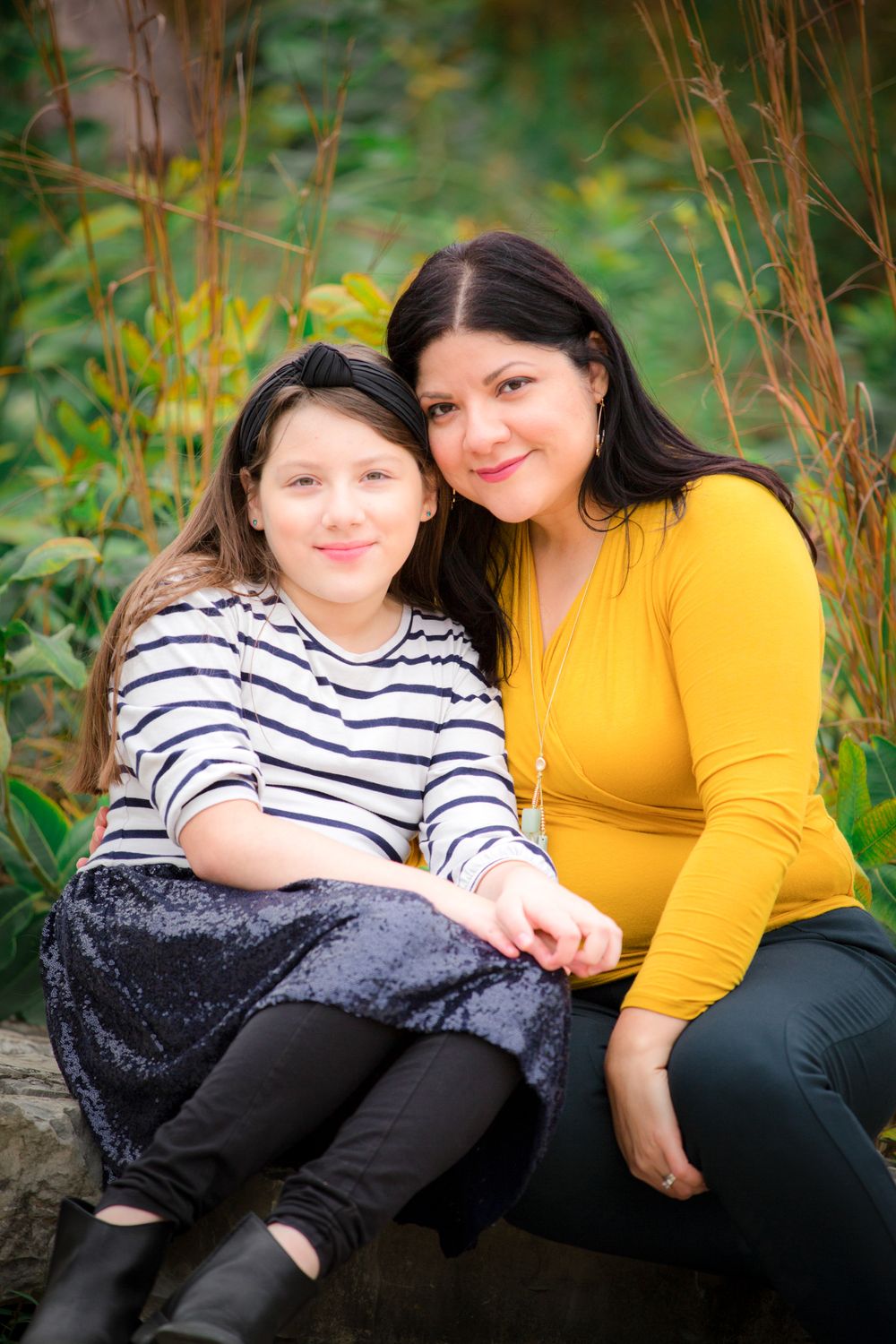 Two people share a tender moment while sitting outdoors among natural foliage.