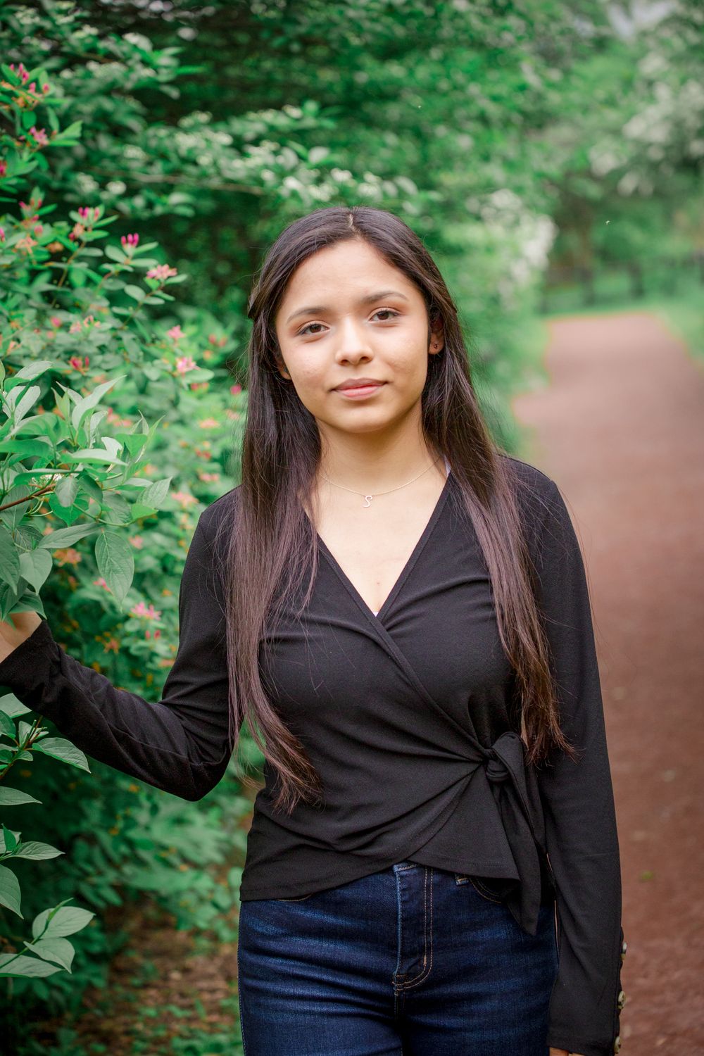 Person in black wrap top poses along garden path surrounded by lush greenery.