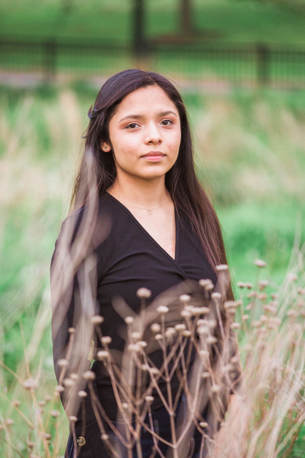 Portrait of person in black wrap dress standing among tall grass with soft natural lighting.