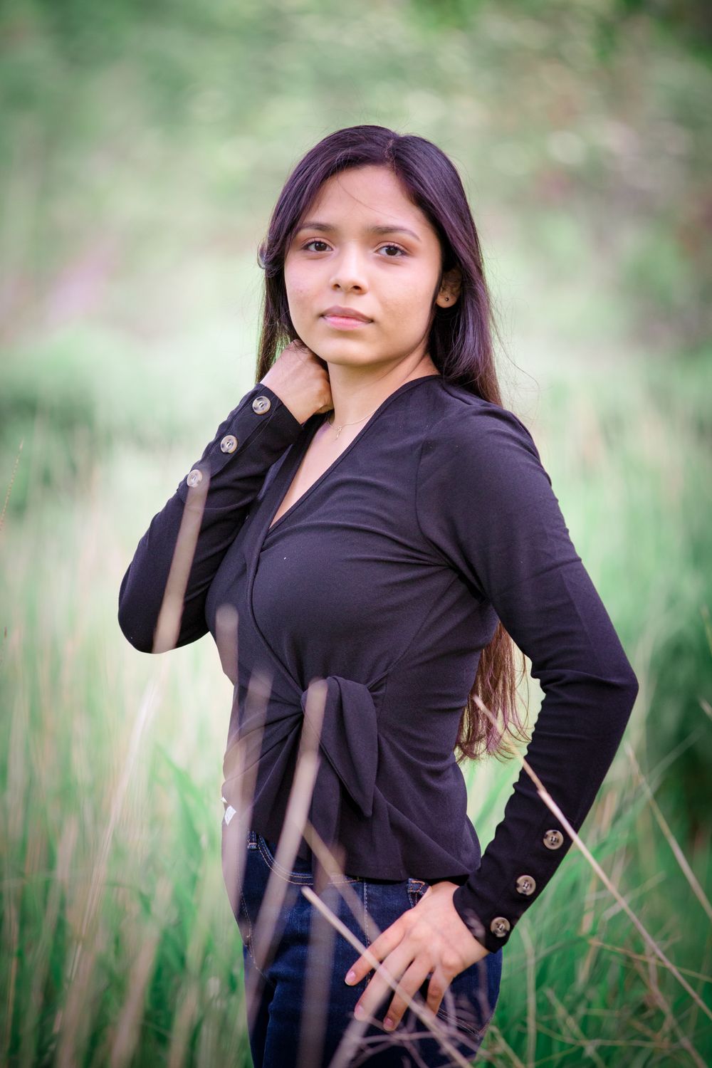 Portrait of person in black wrap top with decorative buttons posing in natural setting.