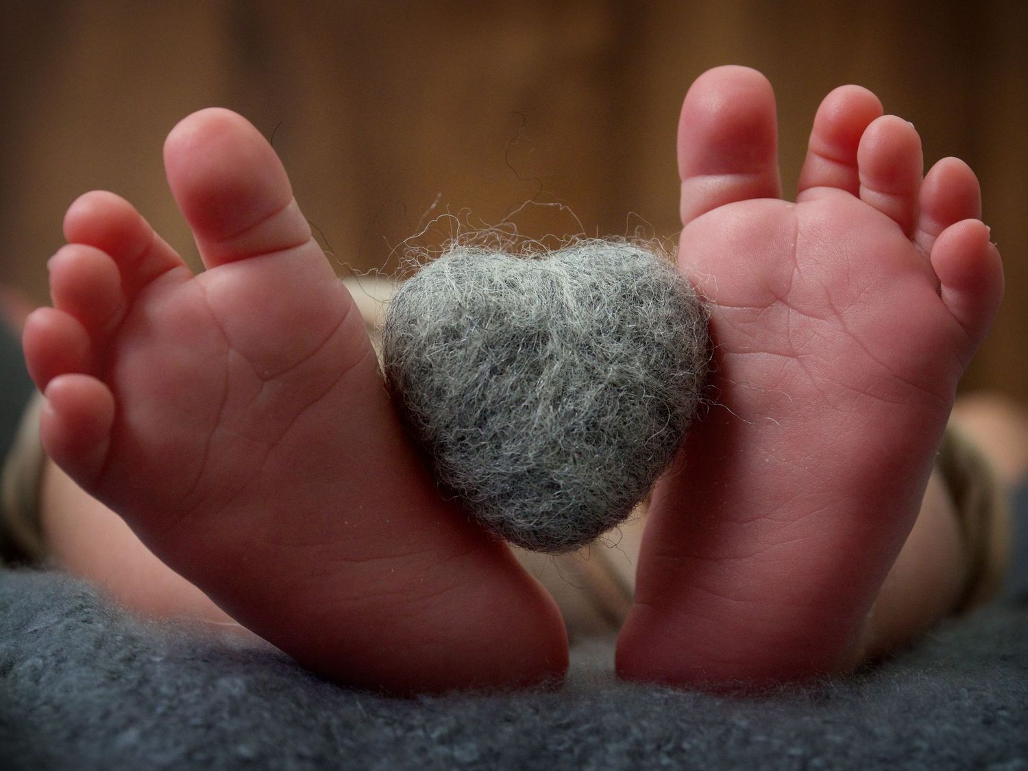 newborn baby feet holding a grey shape woolen heart