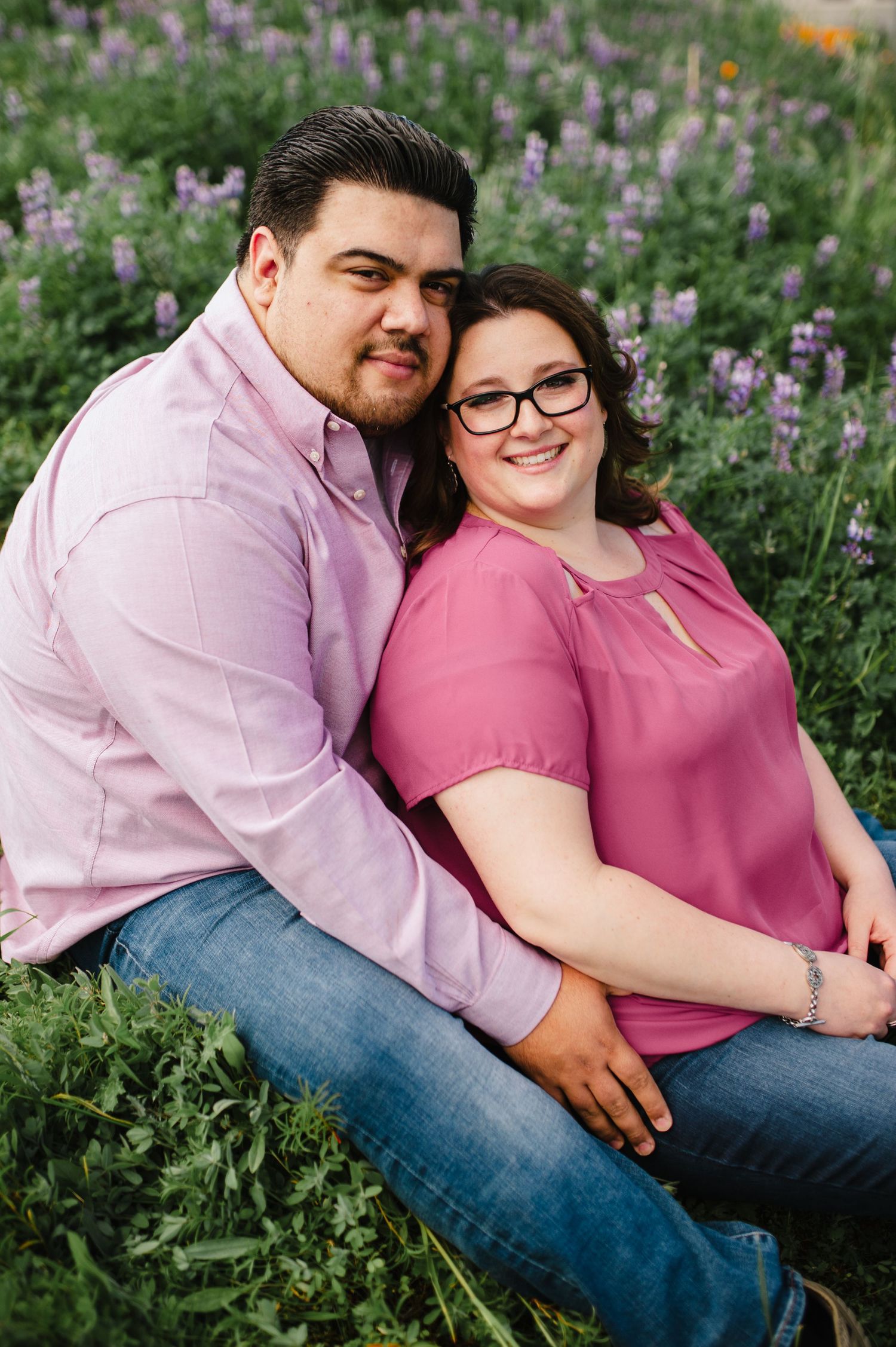Couple sitting together among purple wildflowers during outdoor photo session.