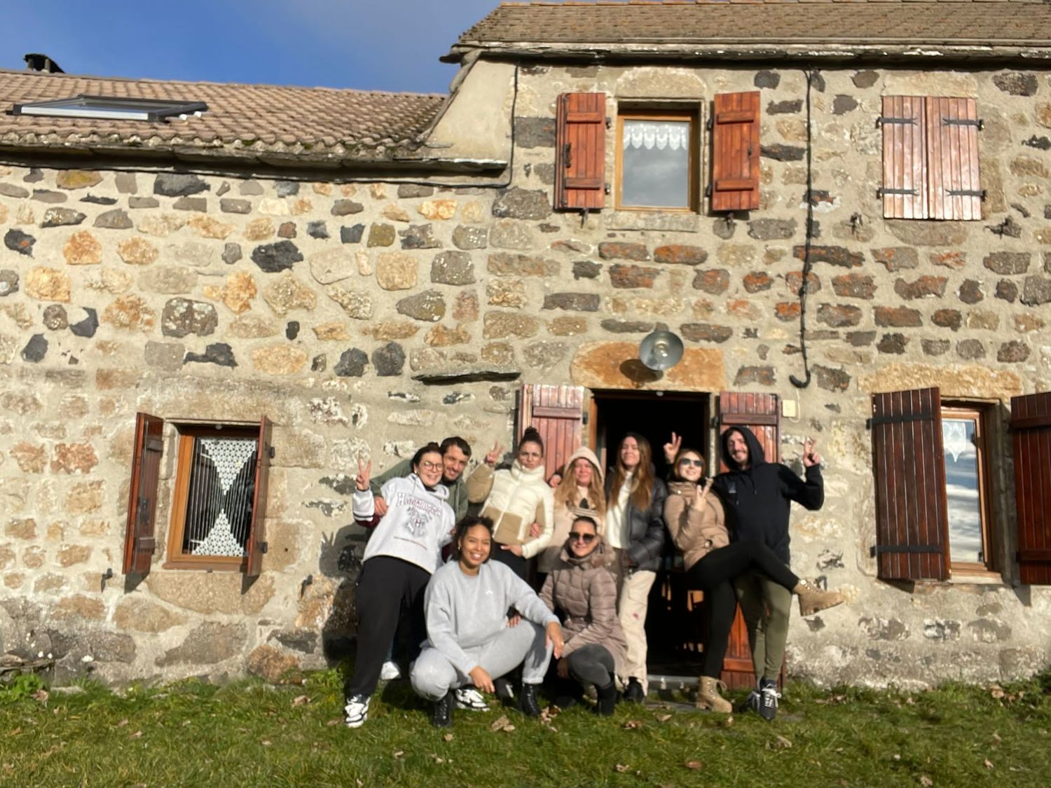 Group photo of friends posing playfully in front of rustic stone farmhouse.