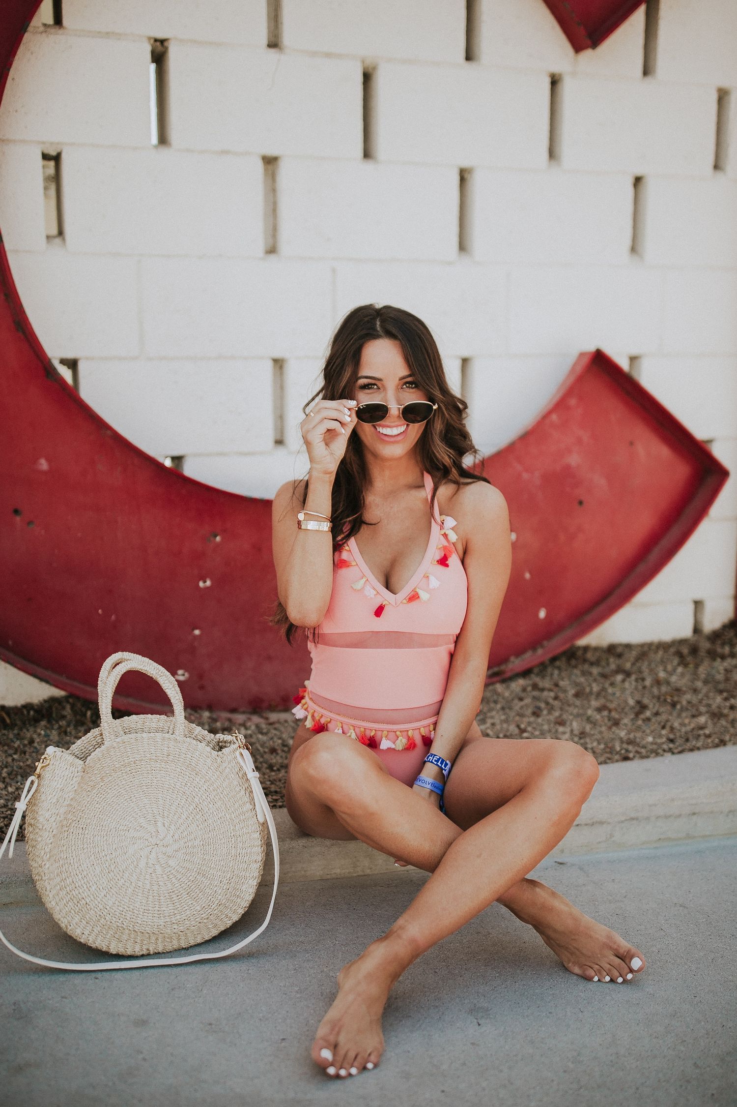Summer poolside fashion photo with pink swimsuit and straw bag against geometric wall.