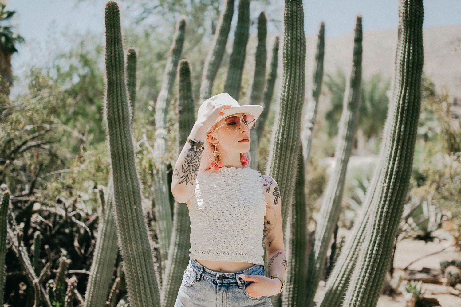 Fashion portrait between tall desert cacti in bright sunlight.