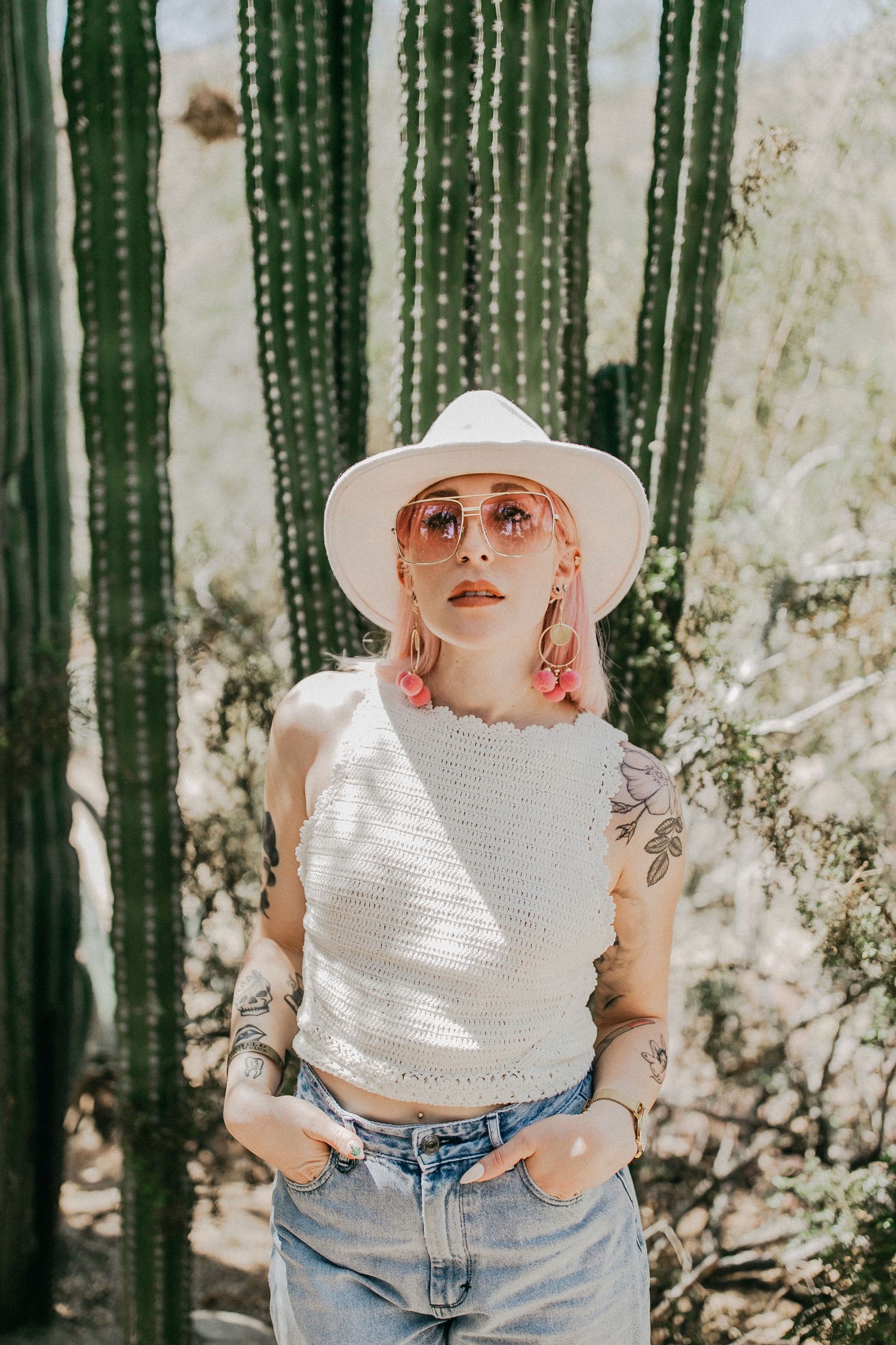Desert fashion scene with white crochet top, hat and jeans against tall saguaro cactus backdrop.