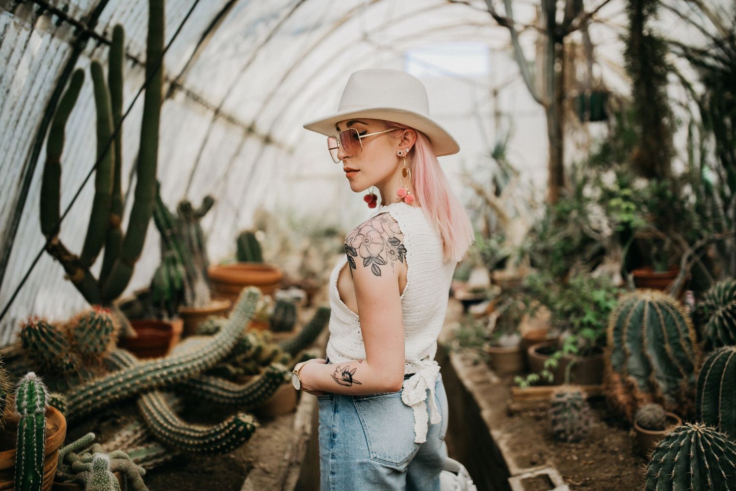 Greenhouse fashion portrait with vintage denim and pink hair among desert plants.