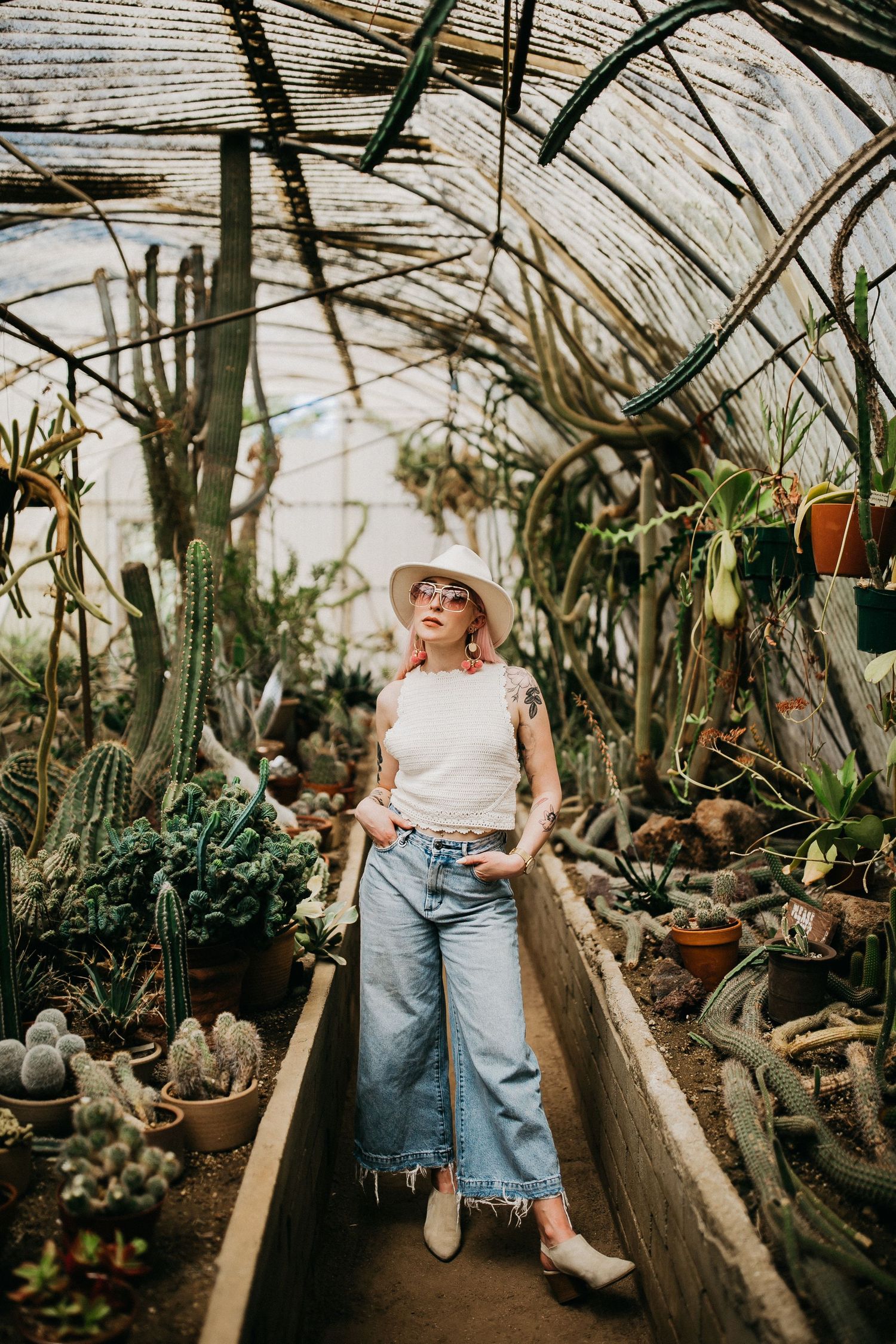 Fashion portrait in greenhouse walkway surrounded by cacti and potted plants.