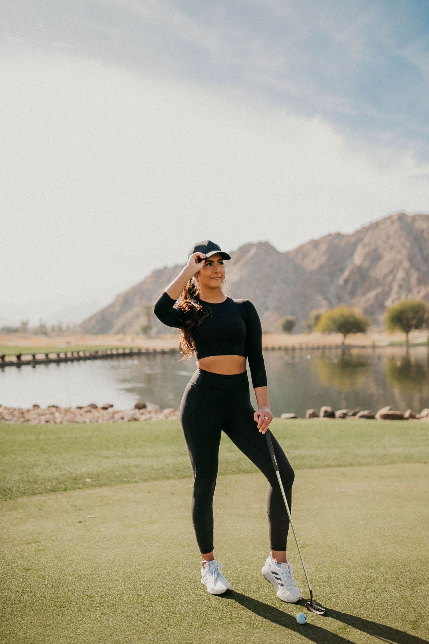 Athletic figure in black outfit on golf course with mountain landscape backdrop.