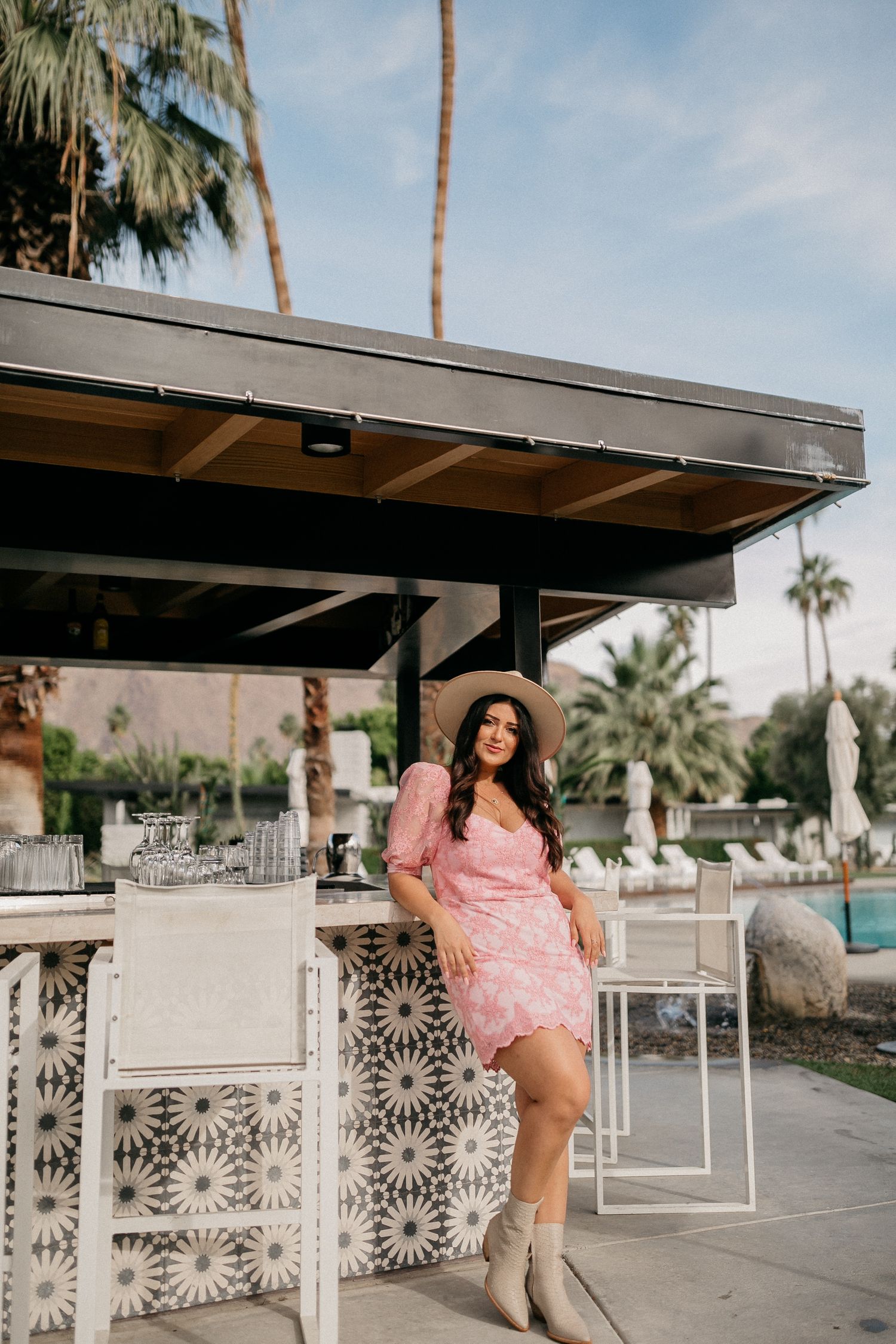 Woman in pink dress poses at outdoor bar area with palm trees.