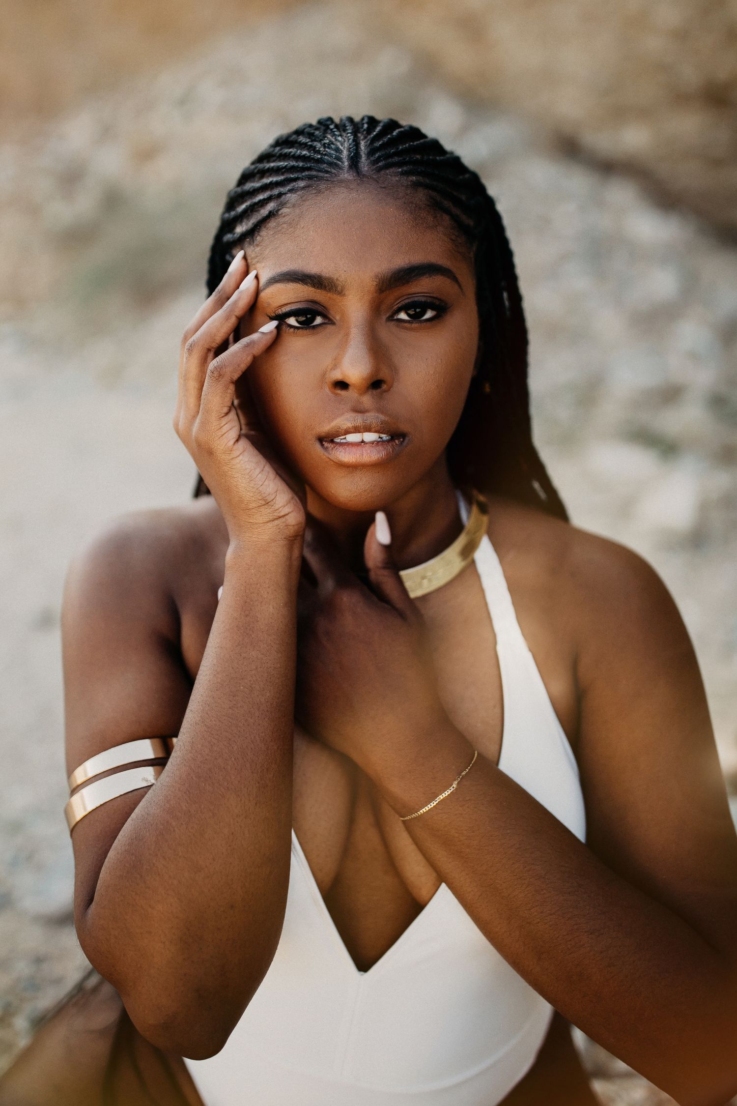 Portrait features white swimsuit and gold accessories against desert backdrop.