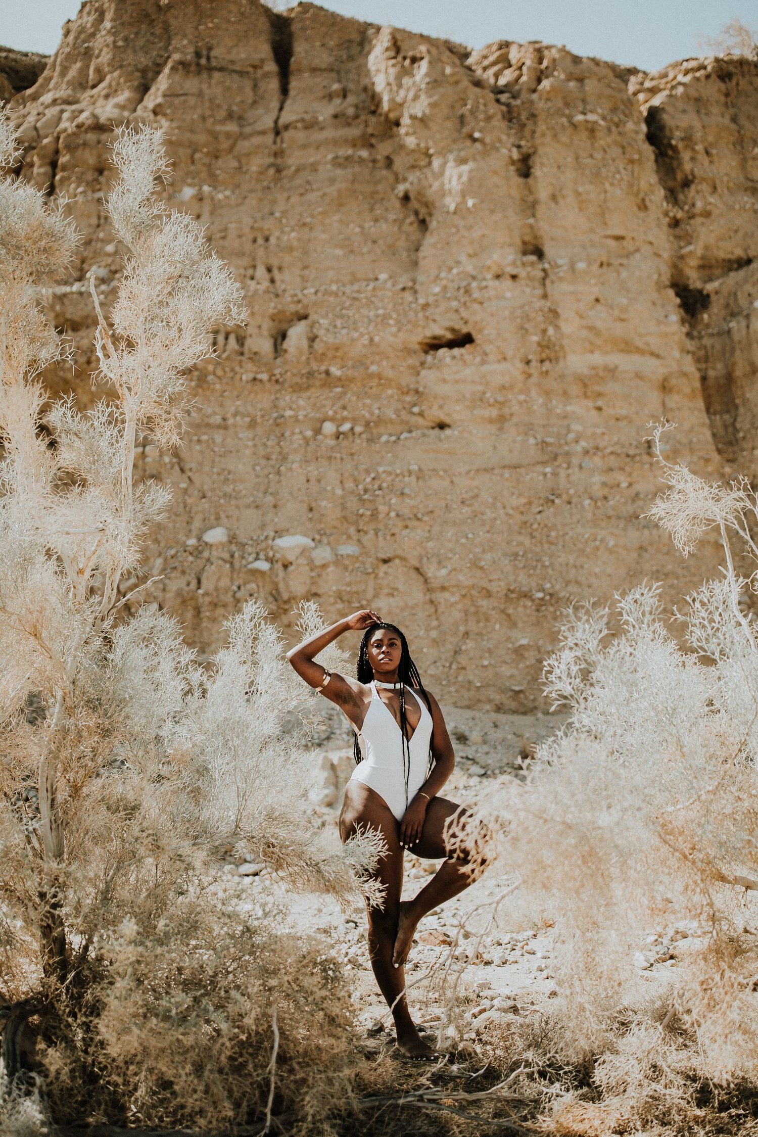 Athletic pose against towering limestone cliff in white bodysuit.