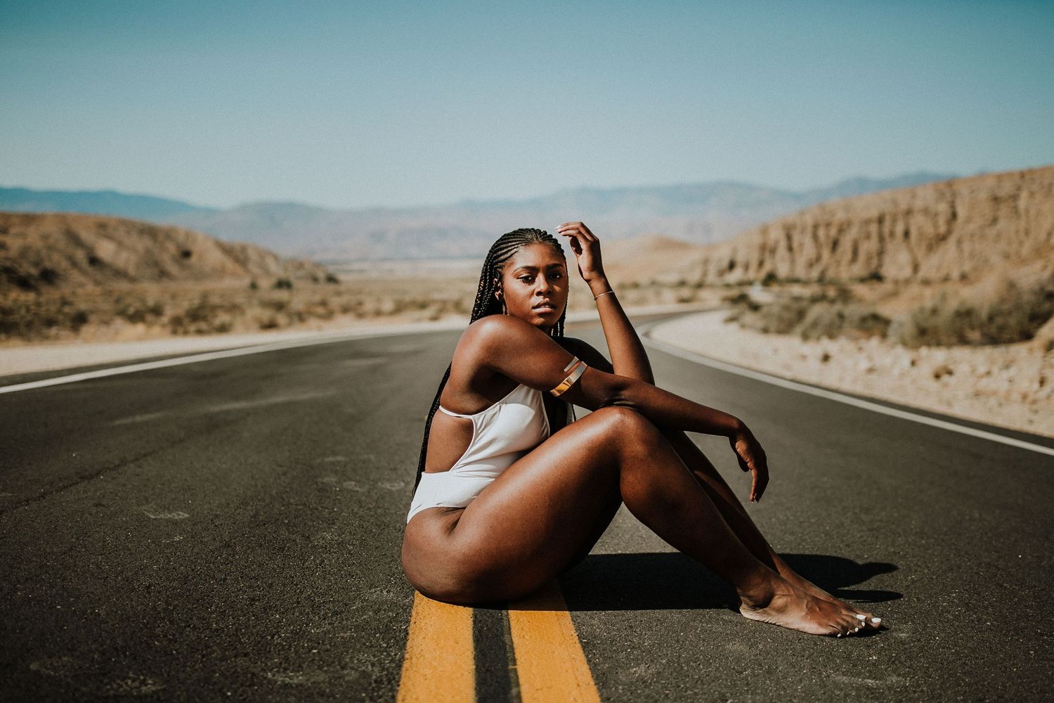 Model in white swimsuit poses on yellow line of desert highway.