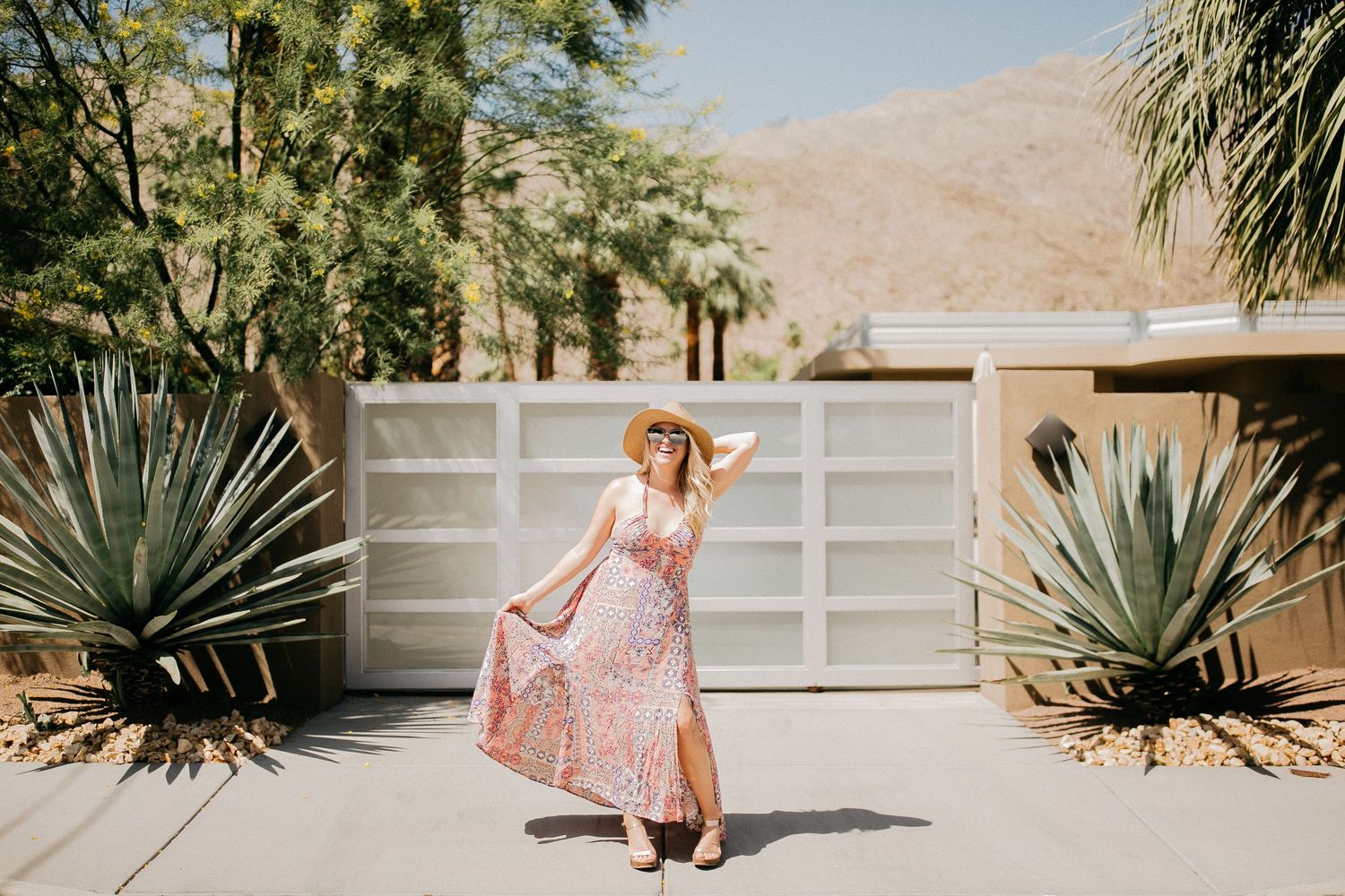 Woman twirls in pink floral dress against modern desert home with agave plants.