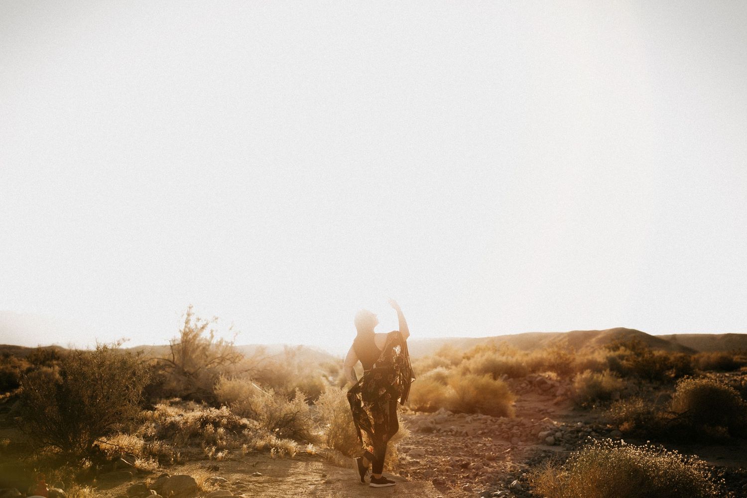 Silhouetted figure walking on desert trail during golden hour.