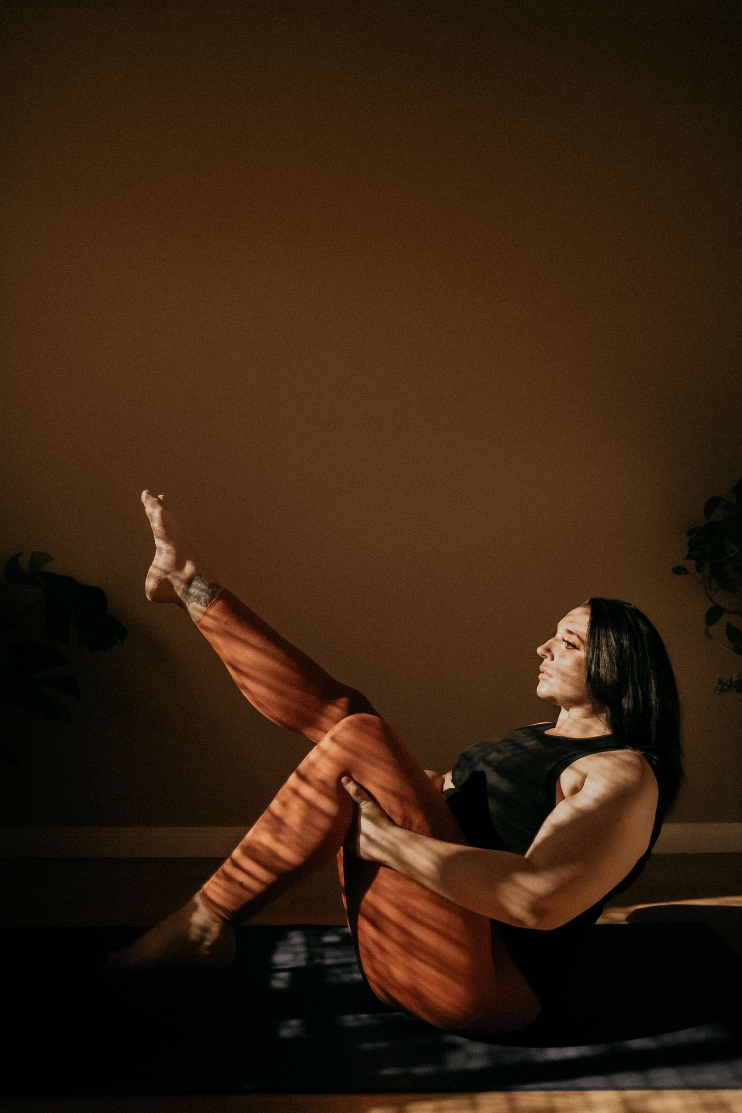 Athletic figure performs yoga pose in orange pants against dark background with dramatic lighting.