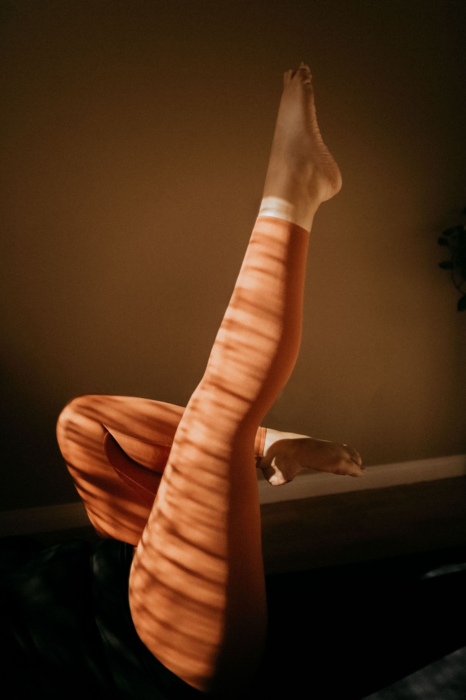Striped shadows fall across legs in orange pants during artistic yoga pose.