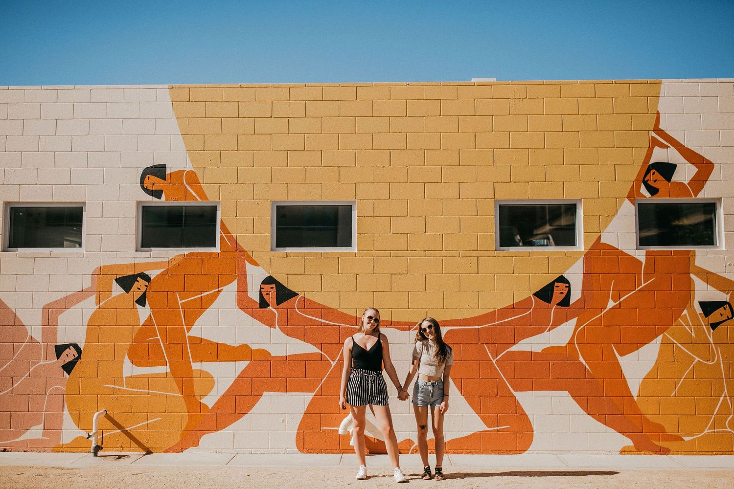 Orange and white mural on building wall featuring dancing figures in geometric style.