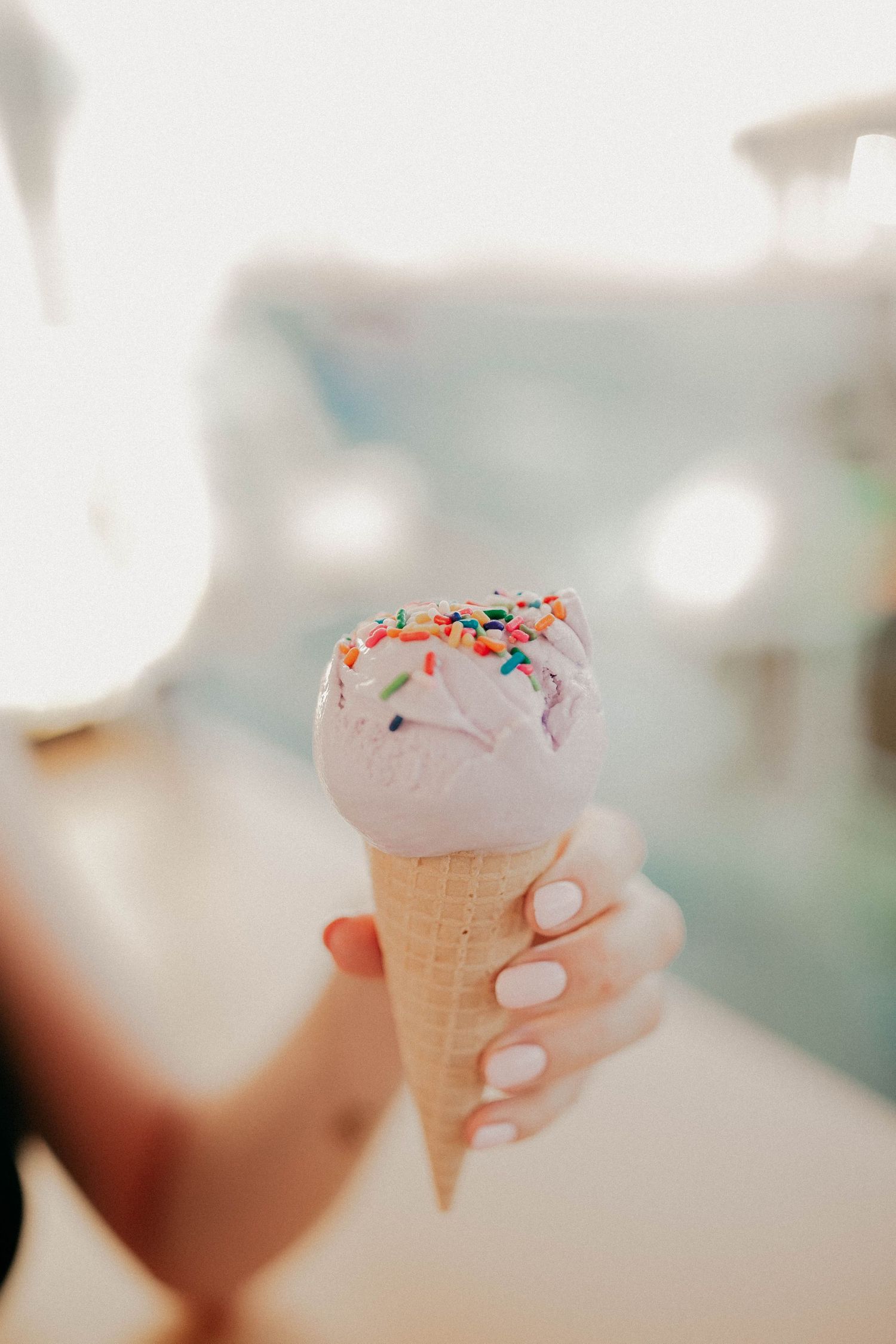 Close-up of vanilla ice cream cone with colorful sprinkles held against blurred background.