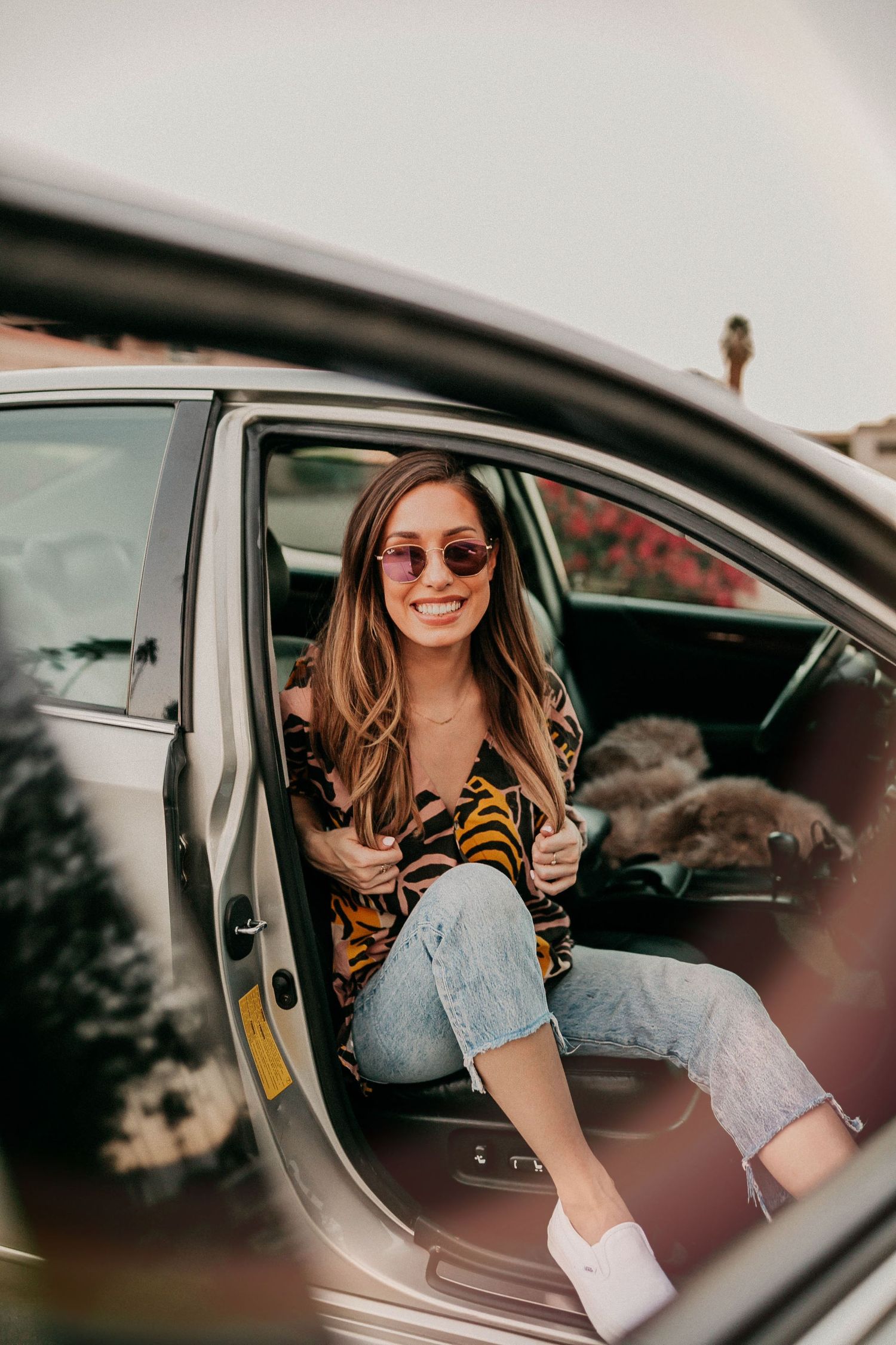 Candid shot of someone sitting in car wearing animal print shirt and sunglasses.