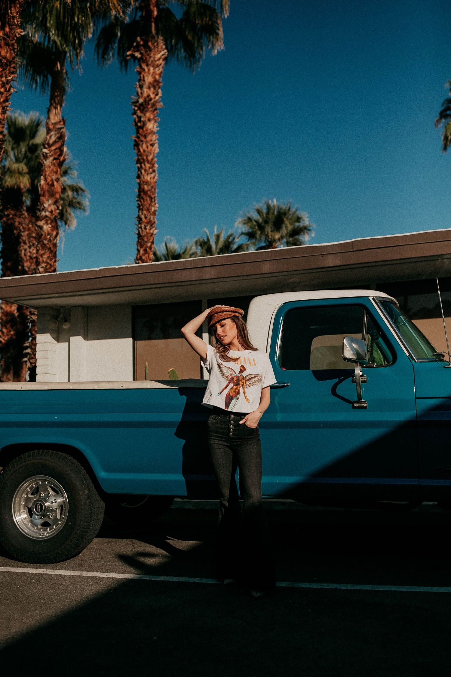 Vintage blue truck parked under palm trees with someone posing beside it.