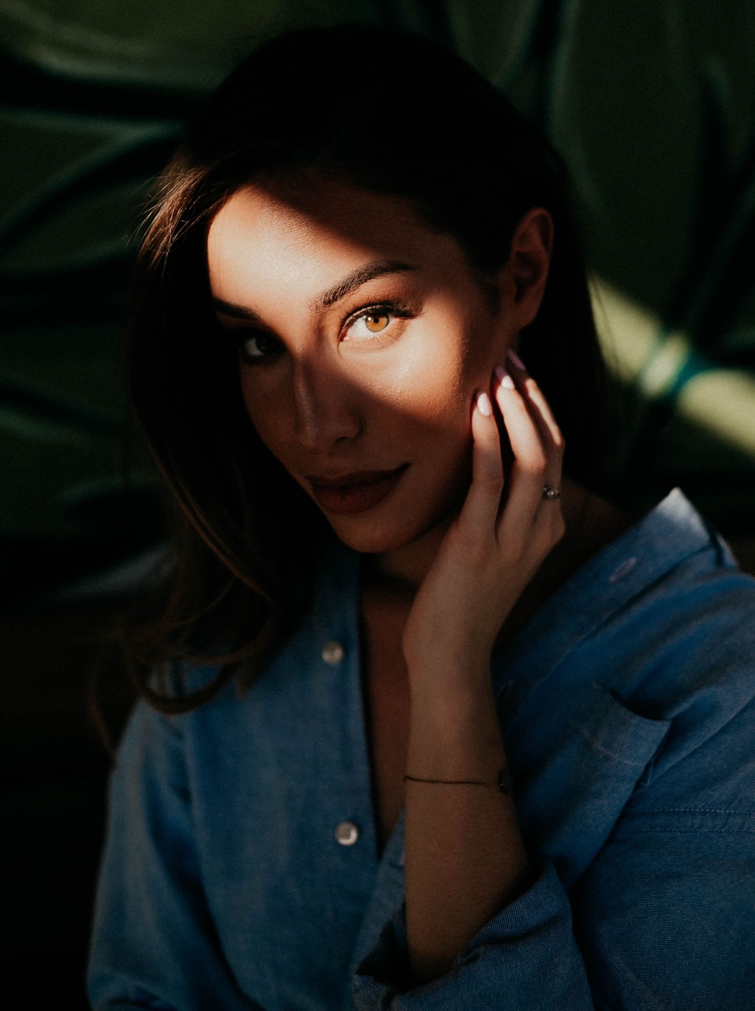 Artistic portrait with dramatic lighting and shadows against green foliage background.