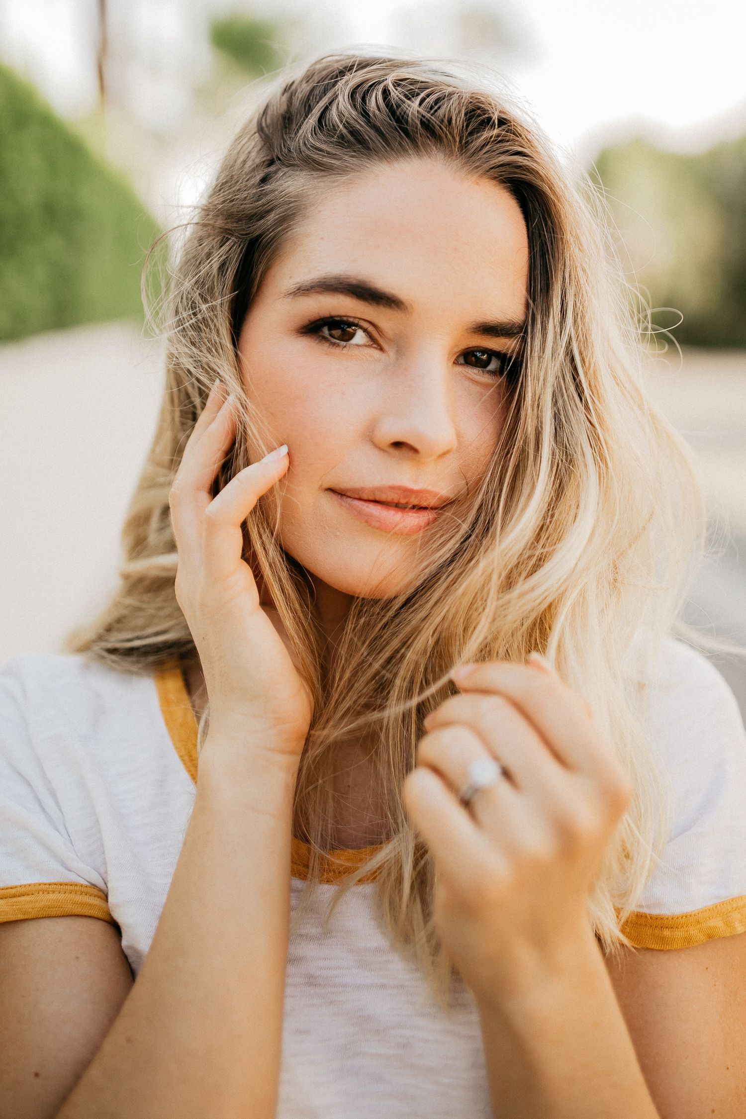 Portrait shot of a woman with blonde hair and natural makeup in a casual white t-shirt with yellow trim.