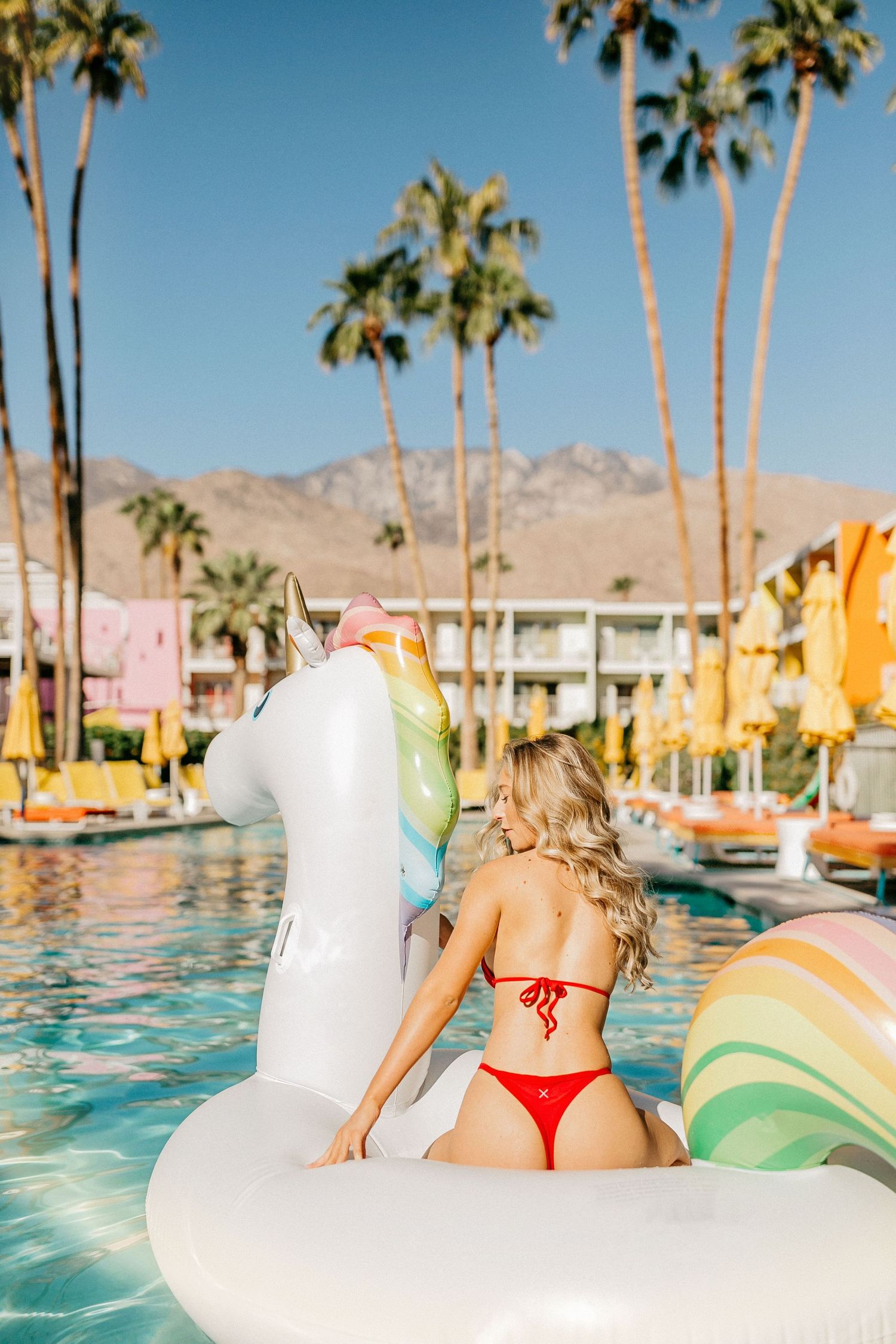 Poolside scene with inflatable unicorn float at a retro-styled desert resort.
