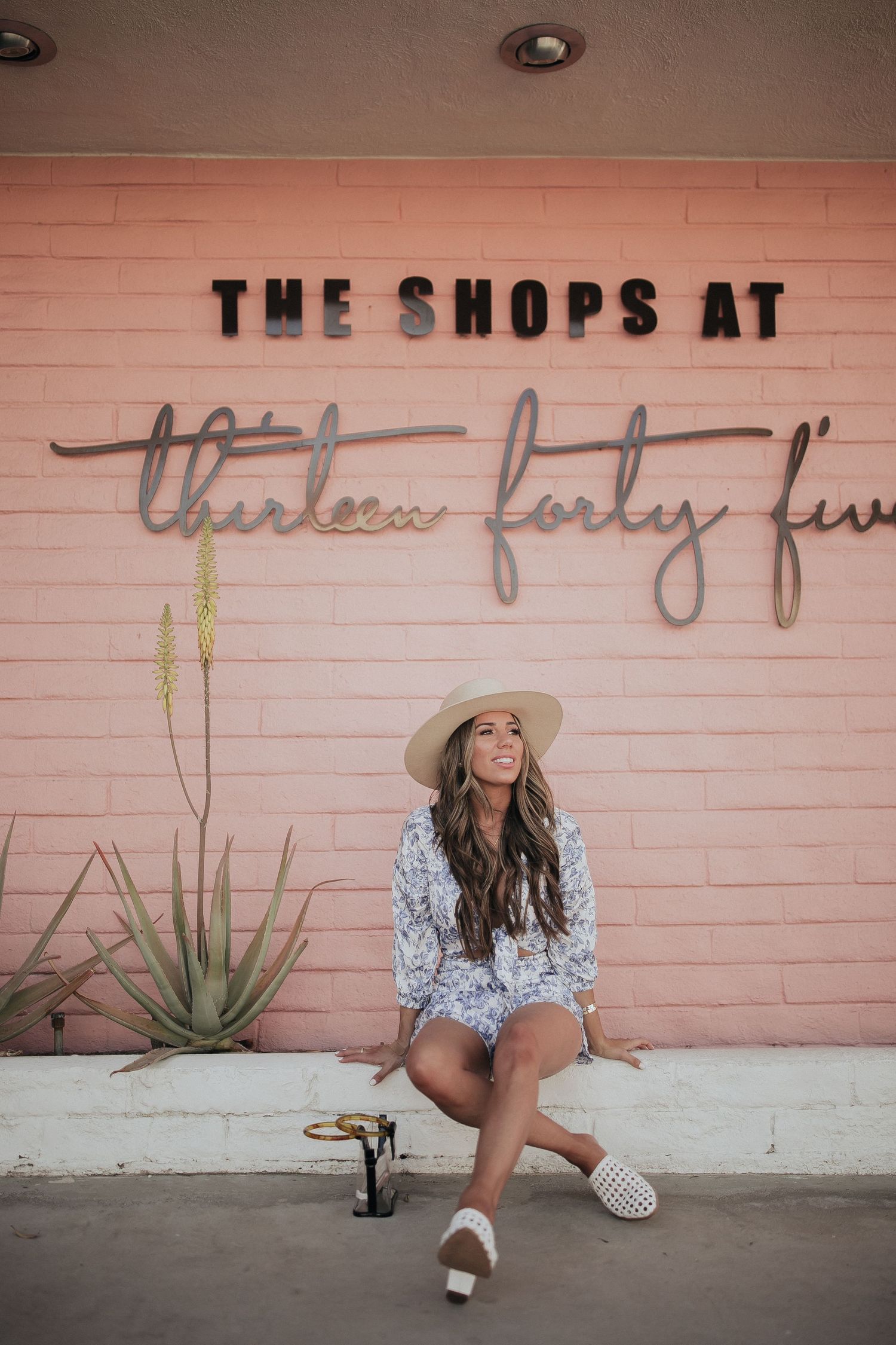 Retro pink wall with 'The Shops at' signage and desert landscaping creates vintage Palm Springs atmosphere.