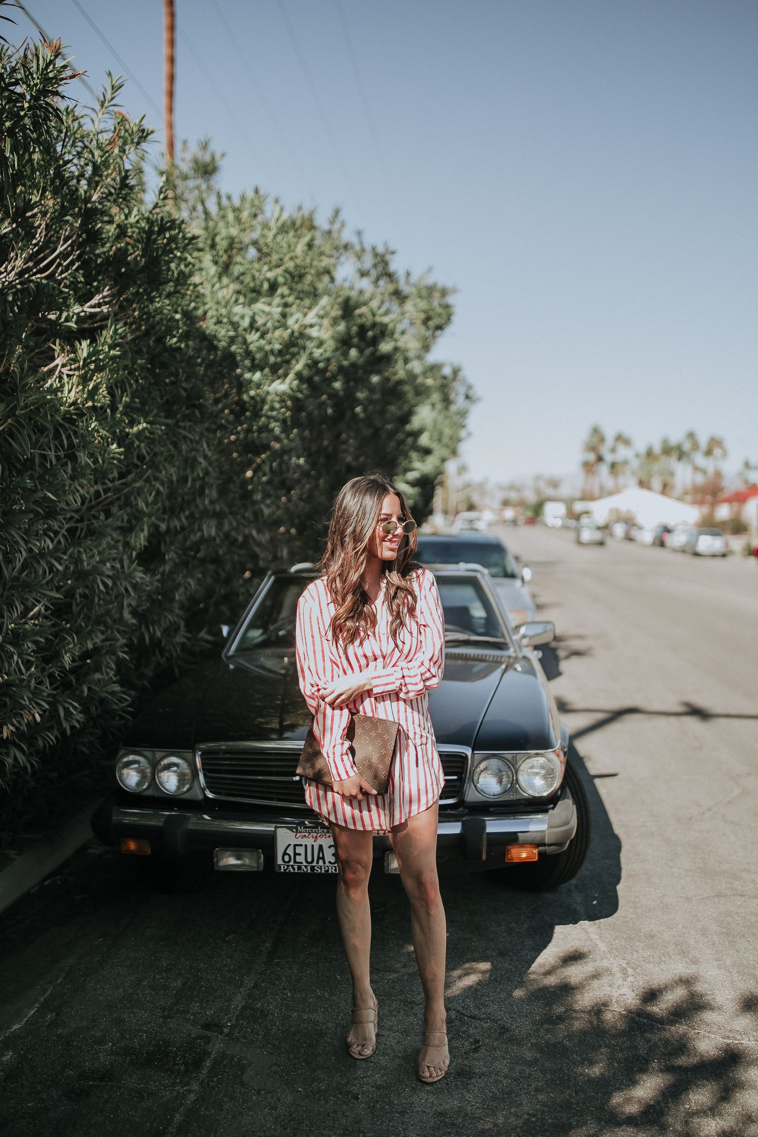 Vintage Mercedes car parked along desert street with lush greenery.