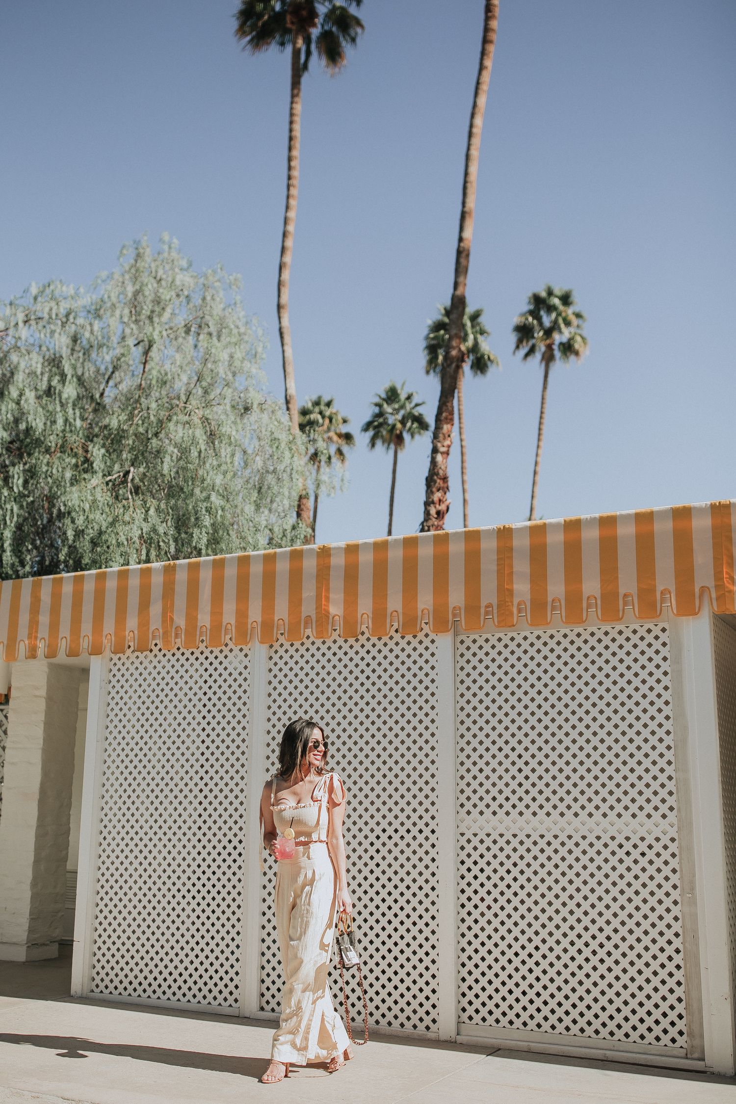 Mid-century modern architecture with lattice wall and orange striped awning under palm trees.