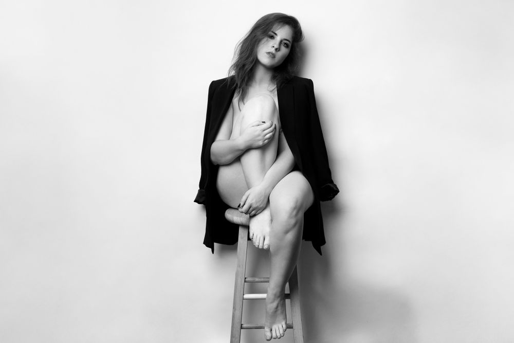 Contemporary fashion portrait with model seated on stool wearing black blazer.