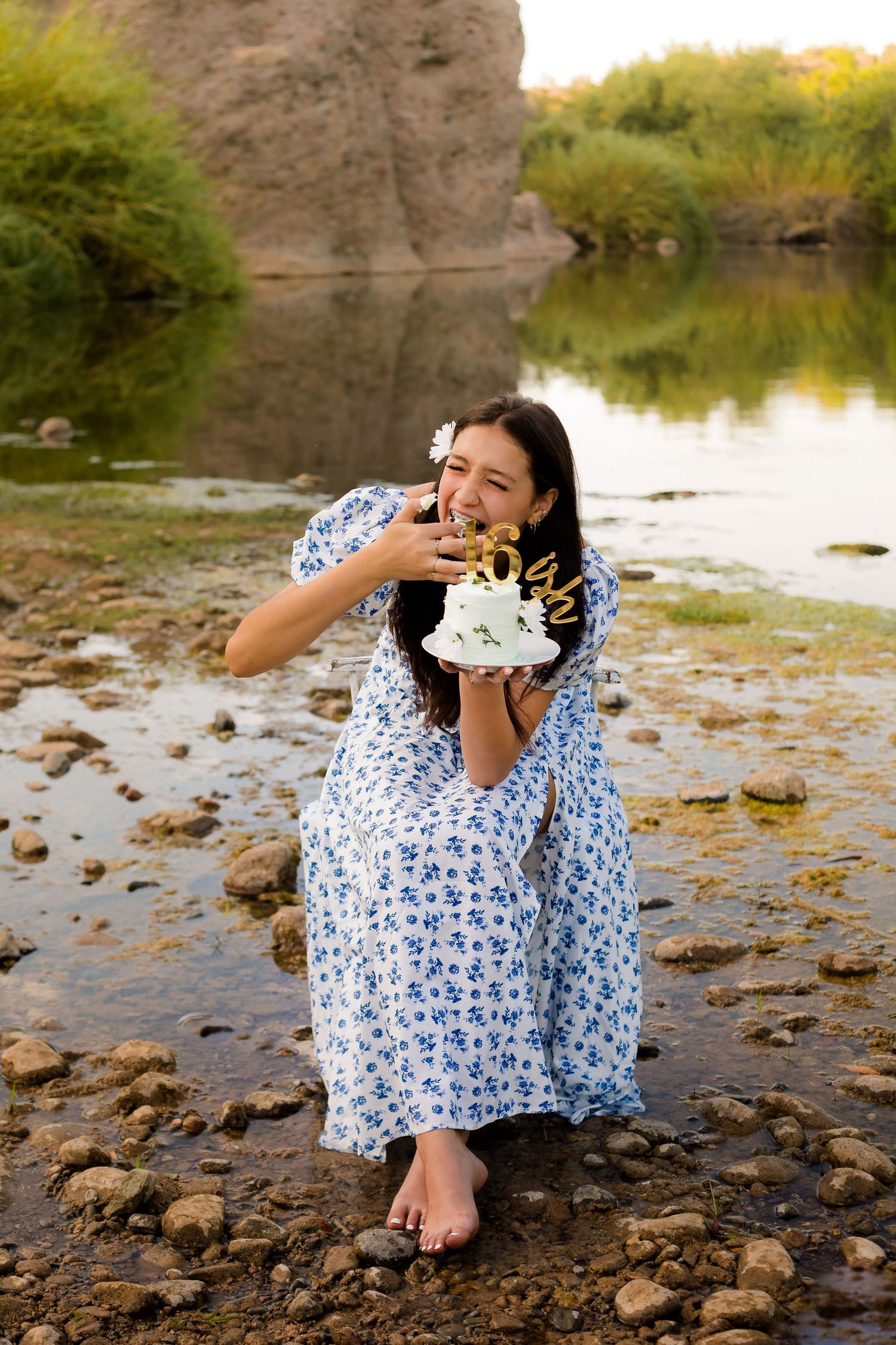 Girl sitting on a chair in the river eating a cake for her sweet sixteen birthday photoshoot in Arizona.