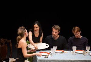 People gathered around a table with plates and glasses in what appears to be a dinner scene.